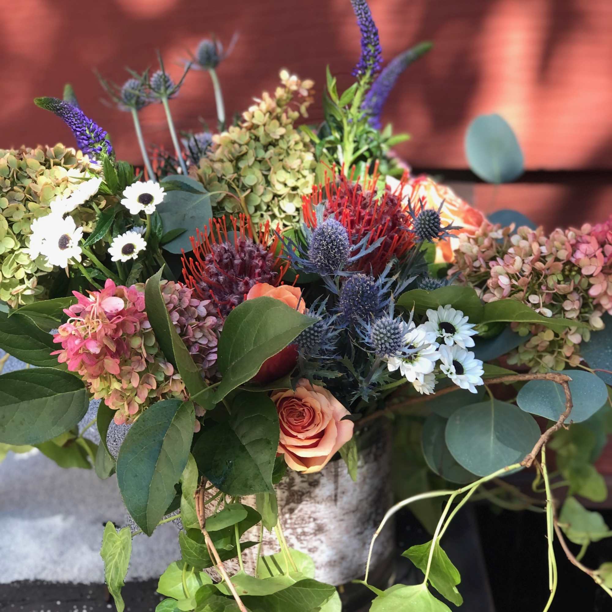 Mixed bouquet with peach roses, white daisies, and purple spikes in a birch vase