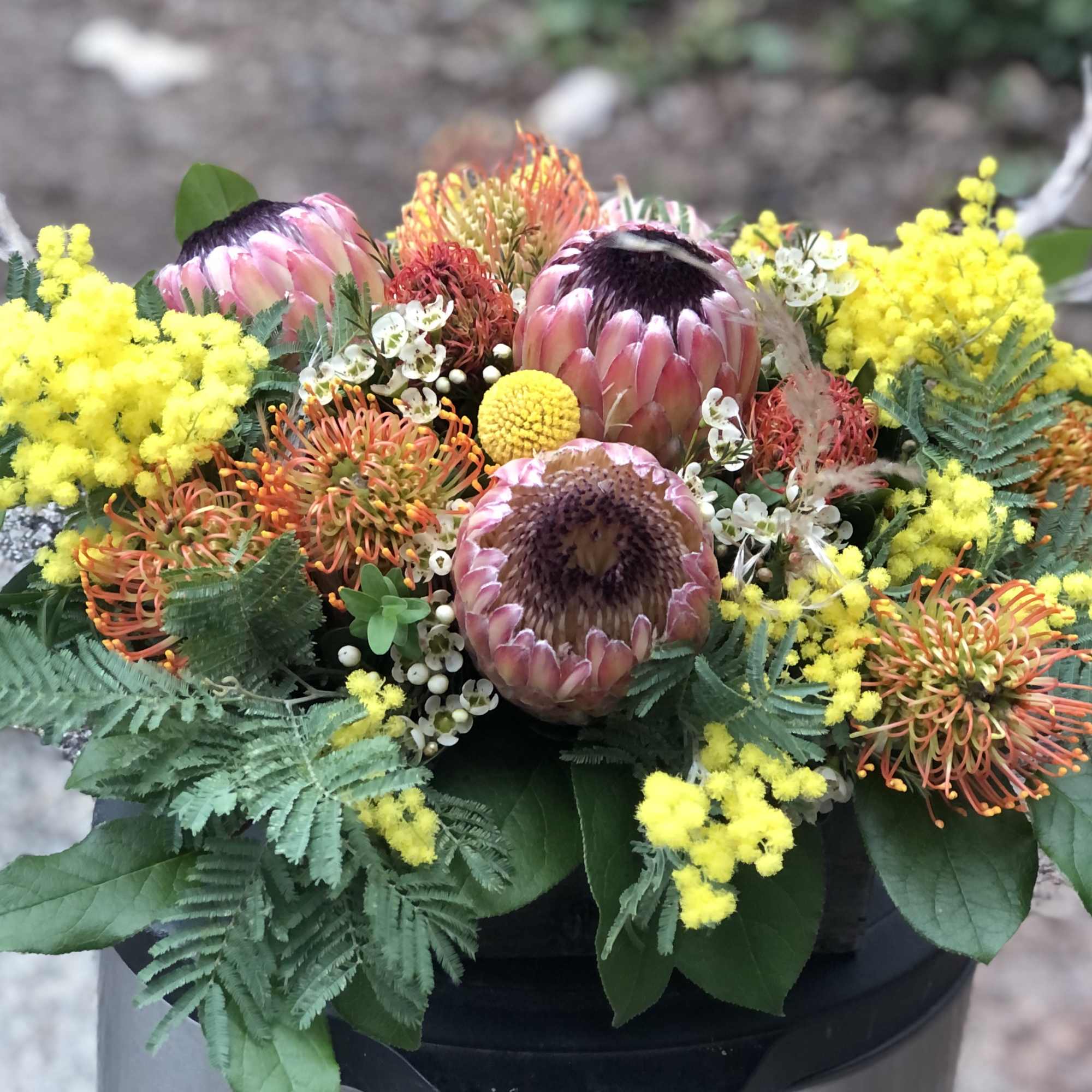 Mixed bouquet with pink protea, yellow mimosa, and orange pincushion blooms