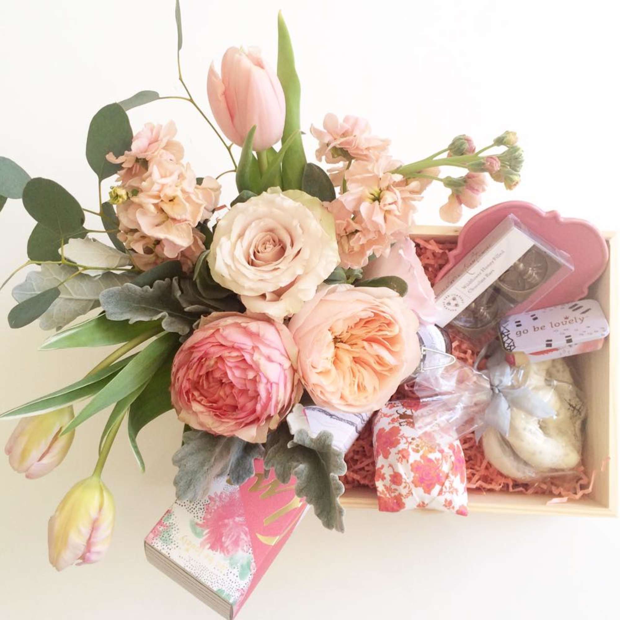 Pastel flower arrangement with roses and tulips beside a gift box of treats