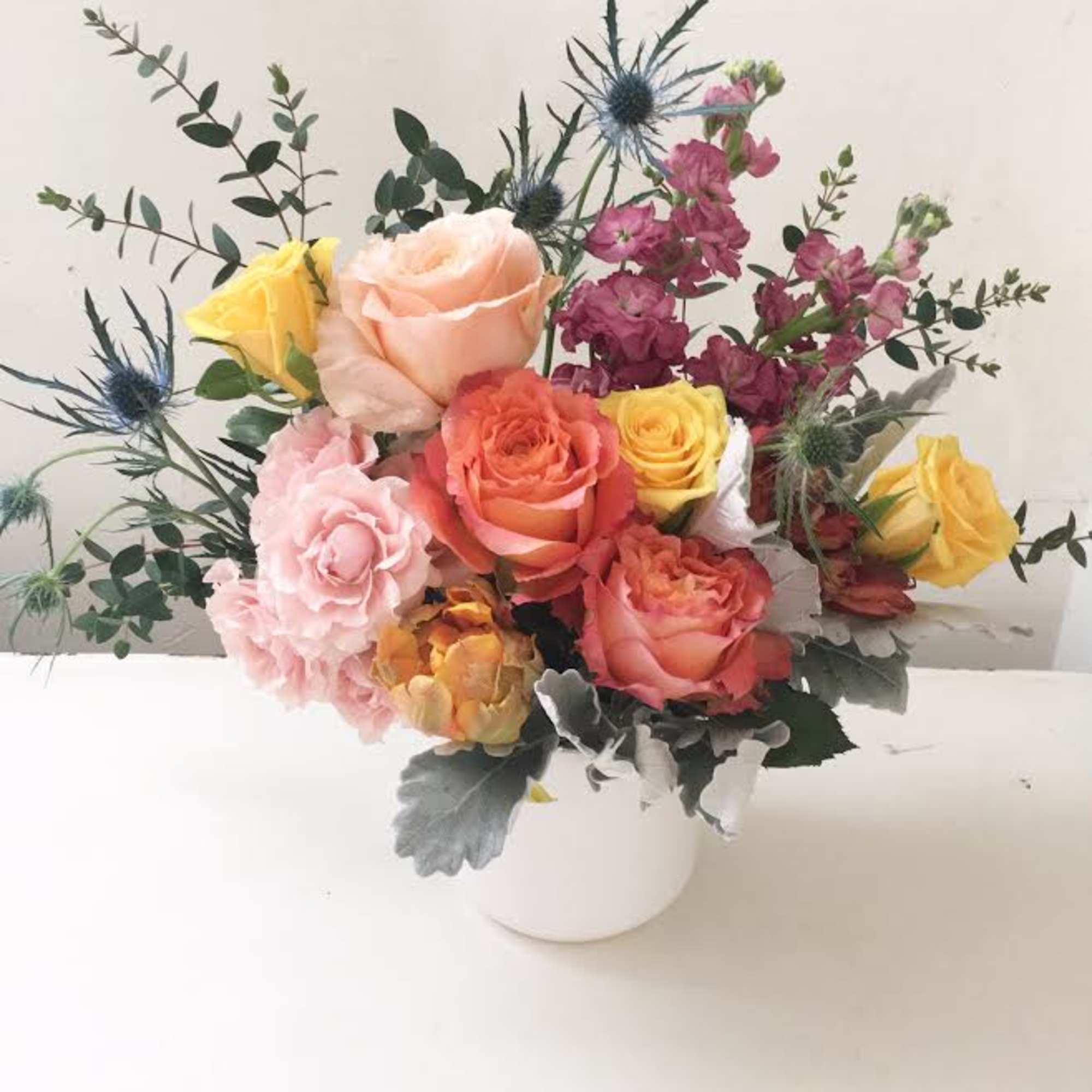 Mixed roses and thistle in a white vase