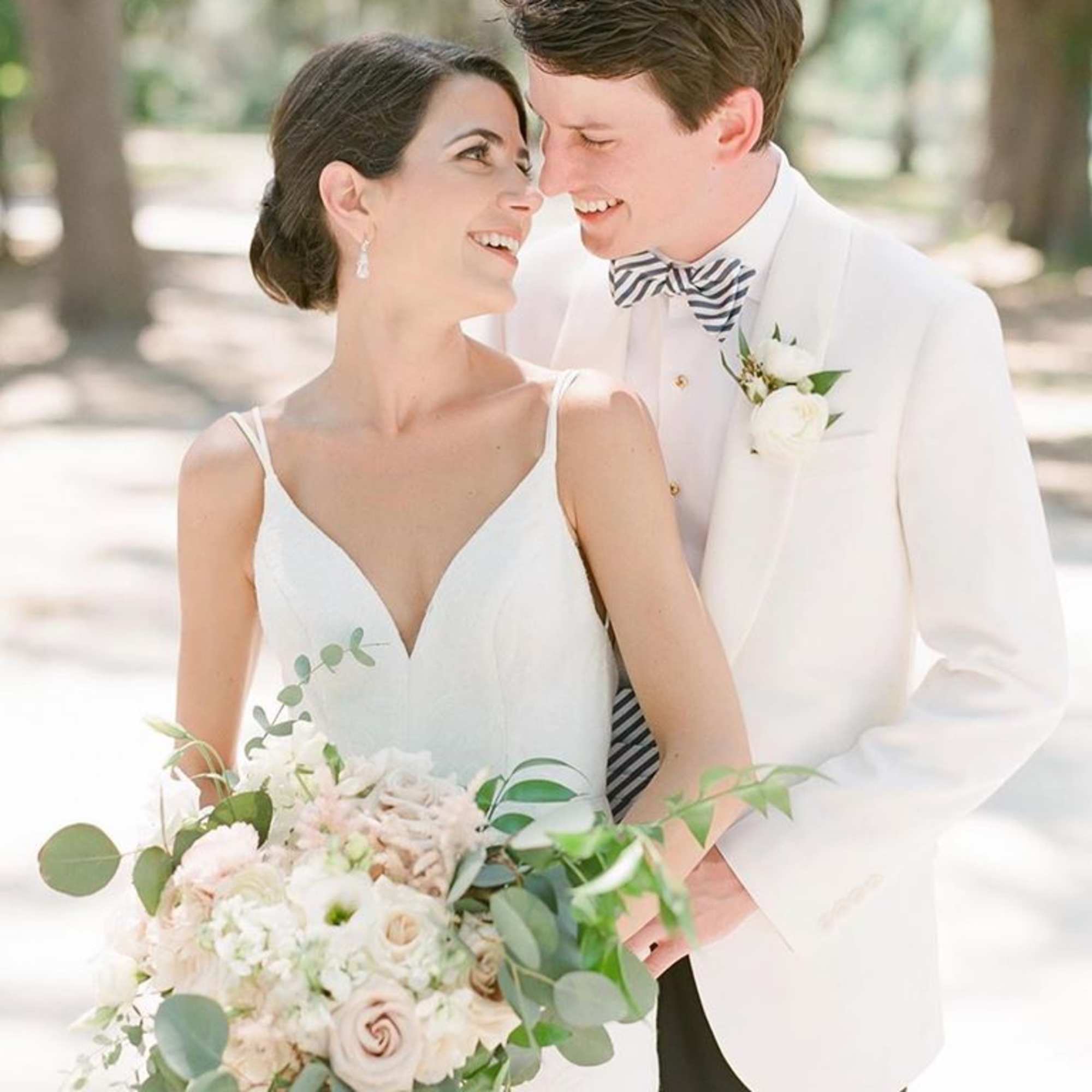 Bride holding a pale bouquet beside a groom in a white jacket