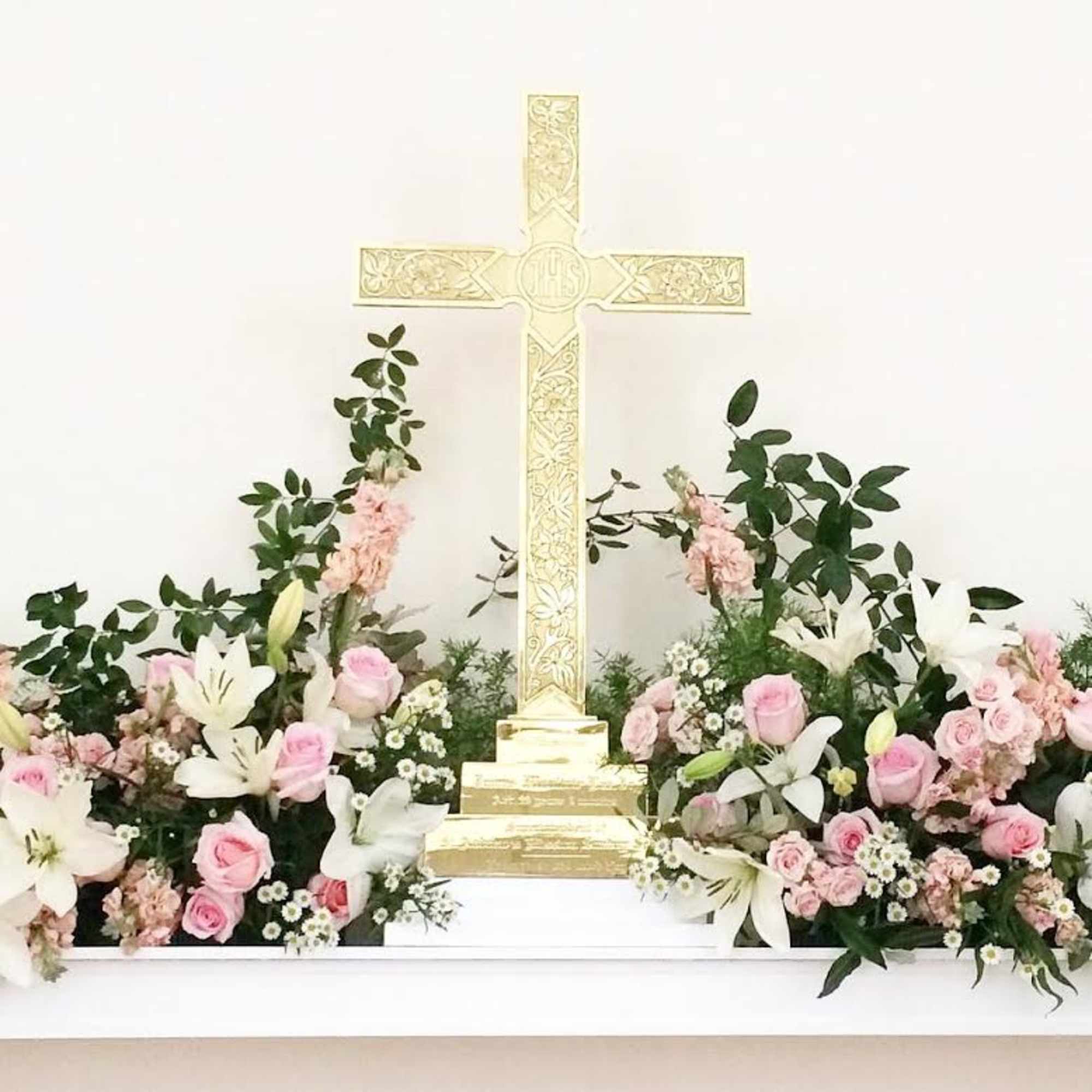 Pink and white floral arrangements around a gold cross