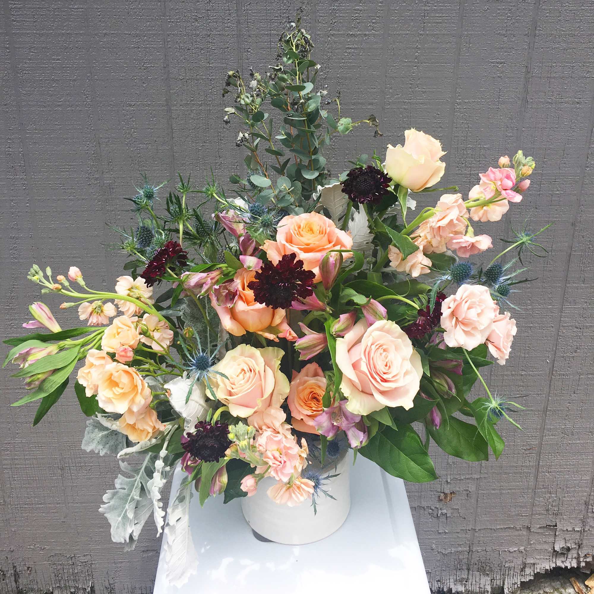 Peach and blush rose arrangement in a white vase with blue thistle accents