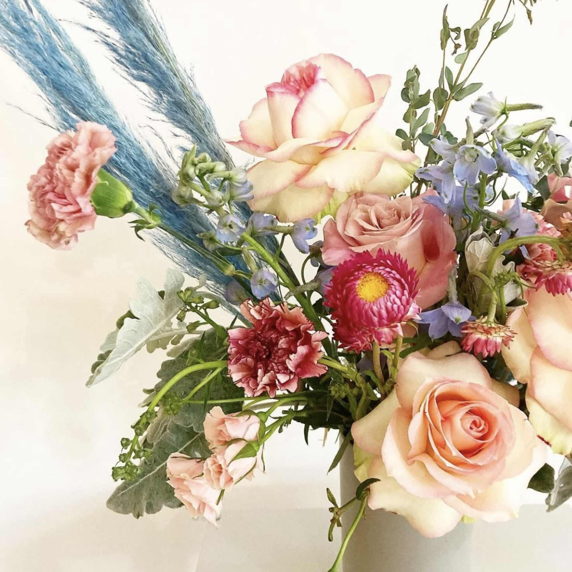 Bouquet of peach roses, pink carnations, and blue flowers in a vase