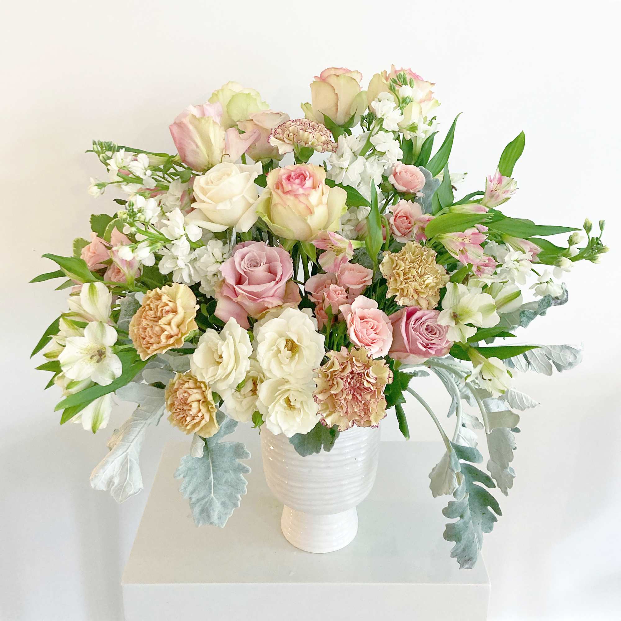 Pastel bouquet of roses, carnations, and white blooms in a white vase