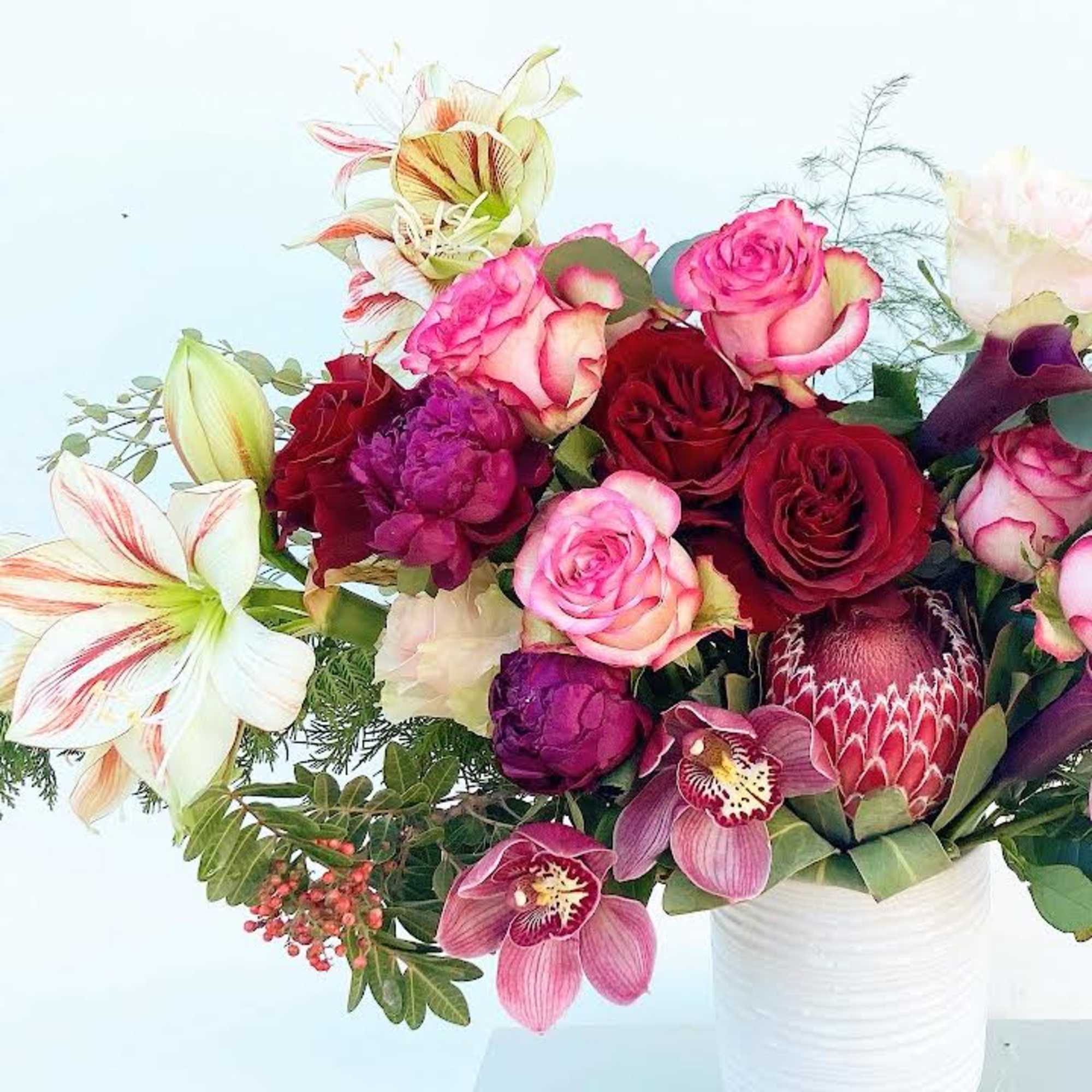 Mixed bouquet of roses, orchids, lilies, and protea in a white vase
