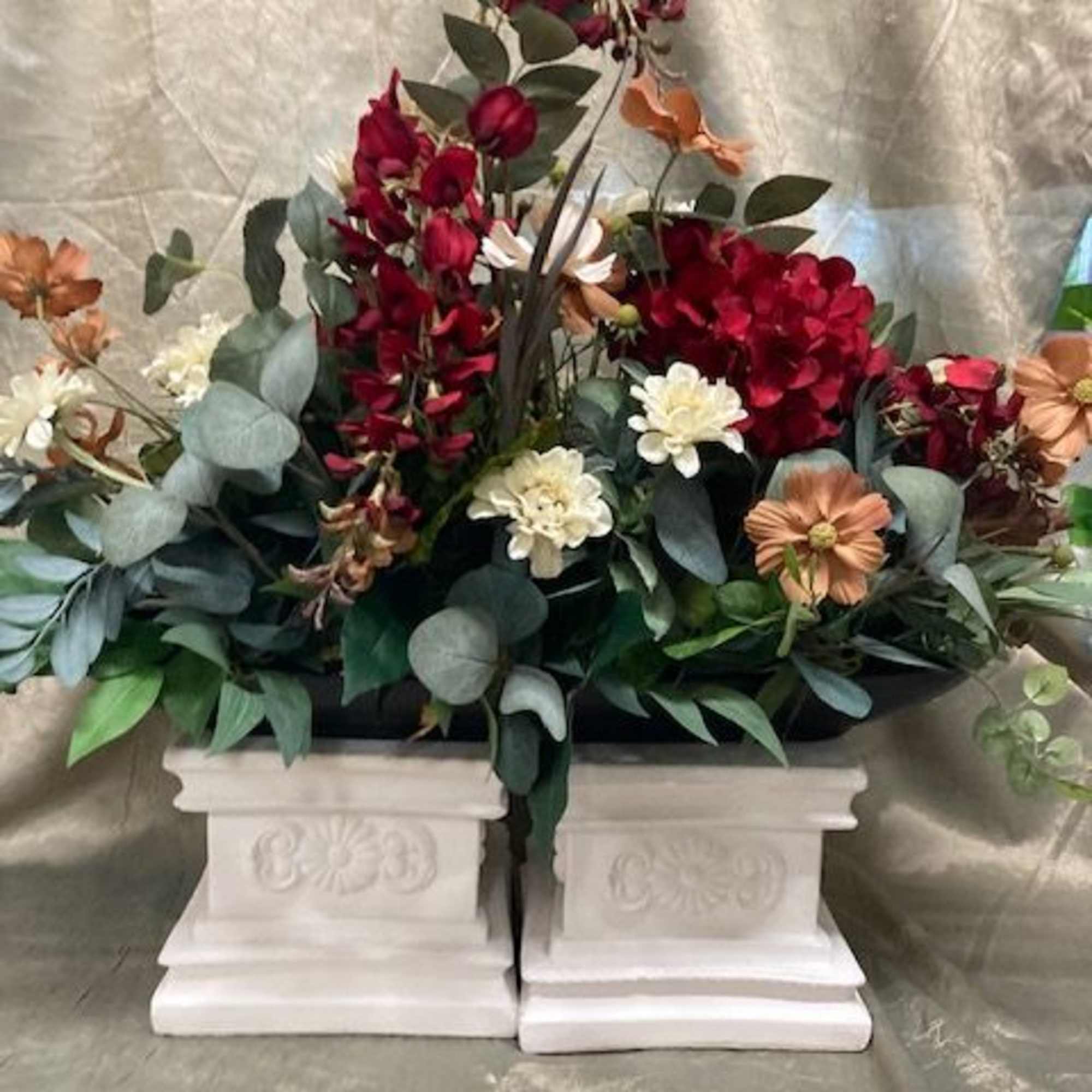 Red and cream floral arrangement in a white pedestal container