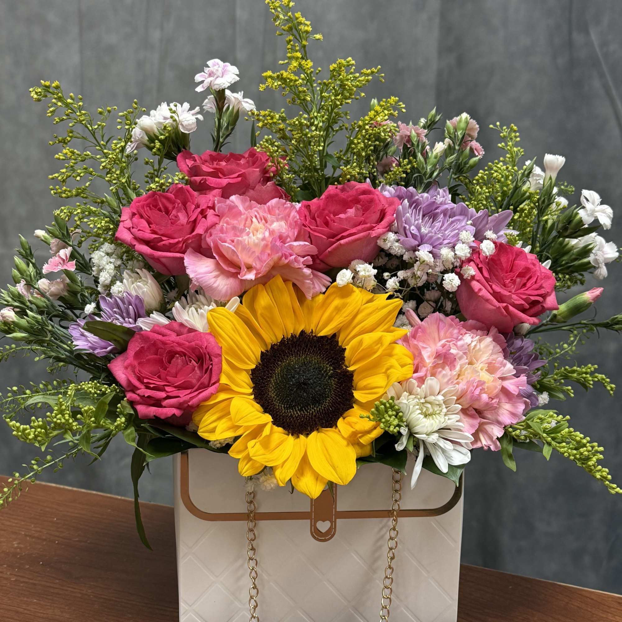 A charming white purse brimming with a joyful sunflower, vibrant carnations, and
