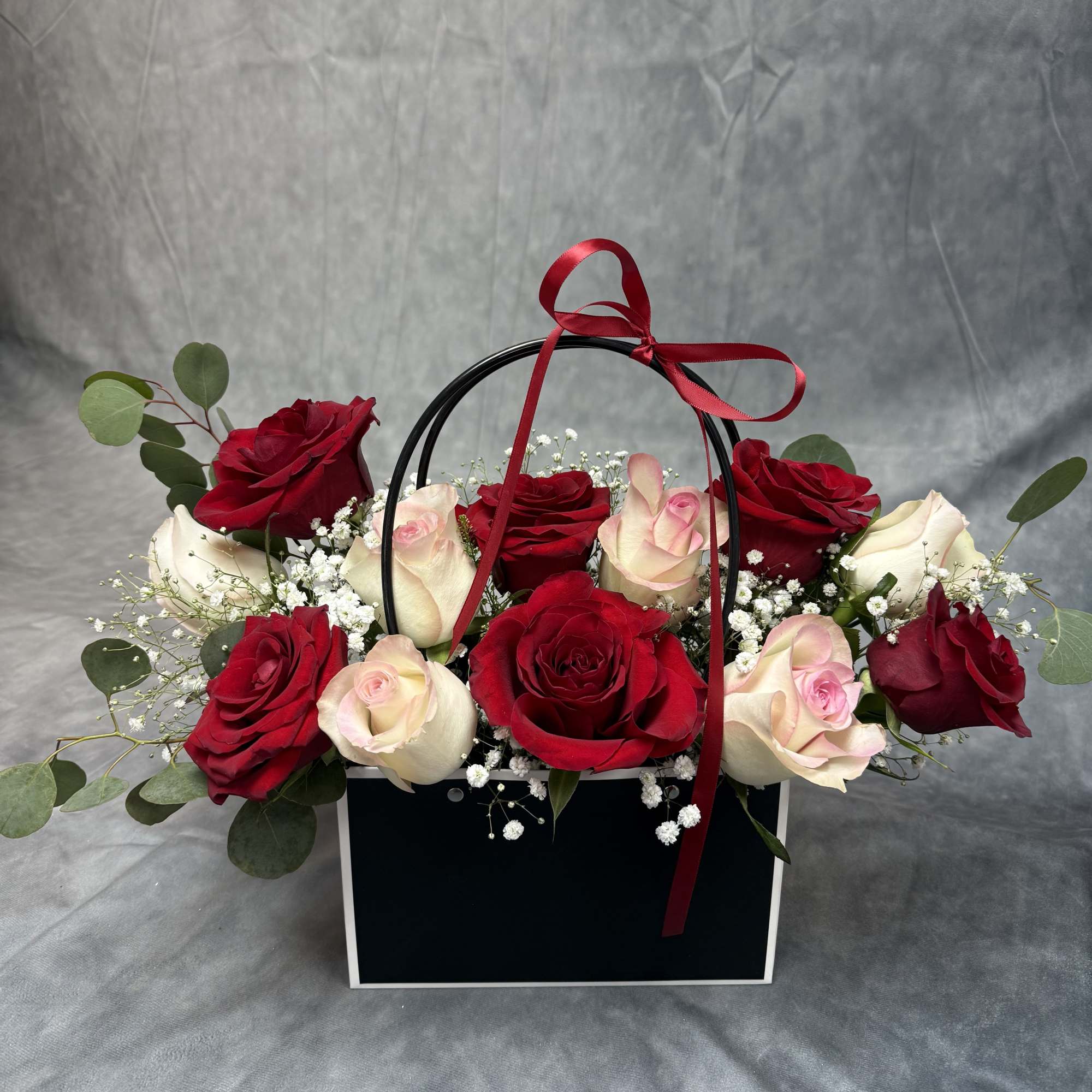 Red and blush roses arranged in a black gift box with a ribbon handle.