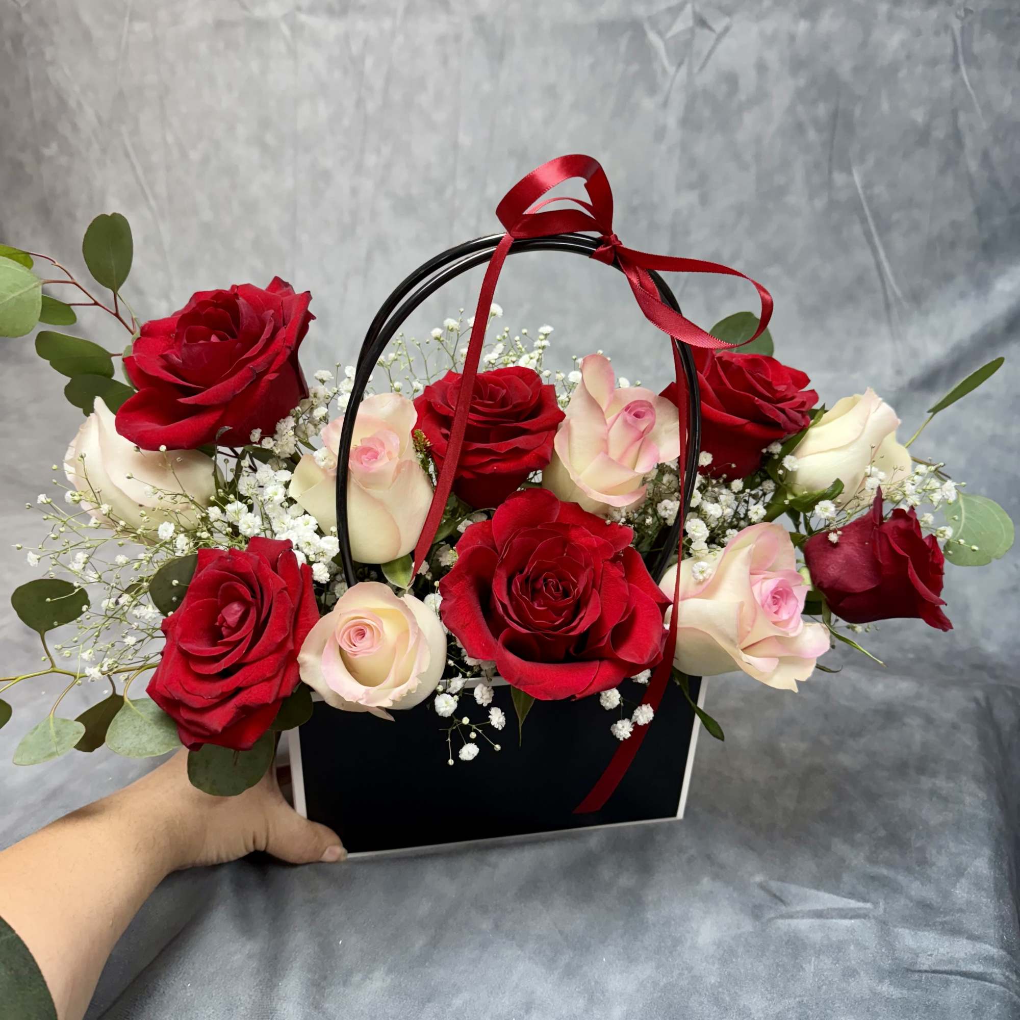 Red and blush roses arranged in a black handled box with a red ribbon