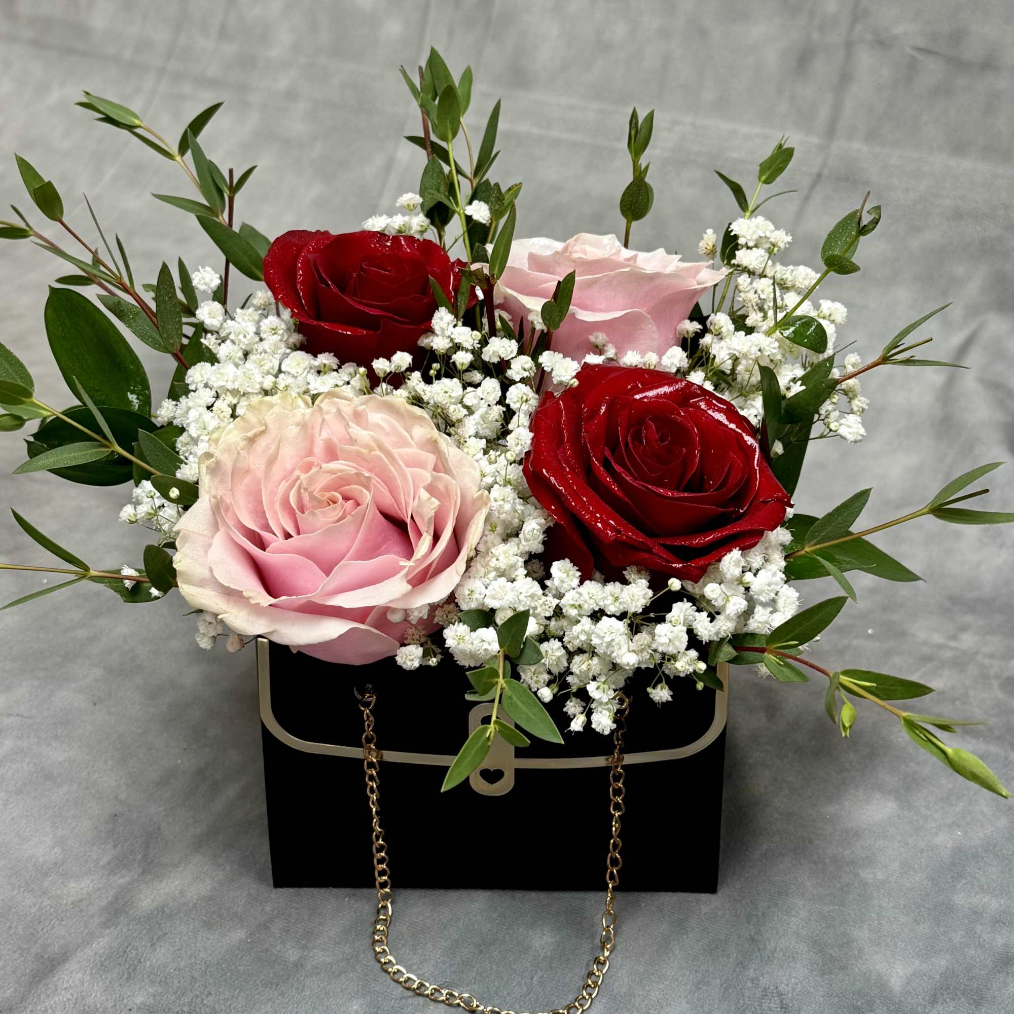 Pink and red roses arranged in a black box with white filler flowers