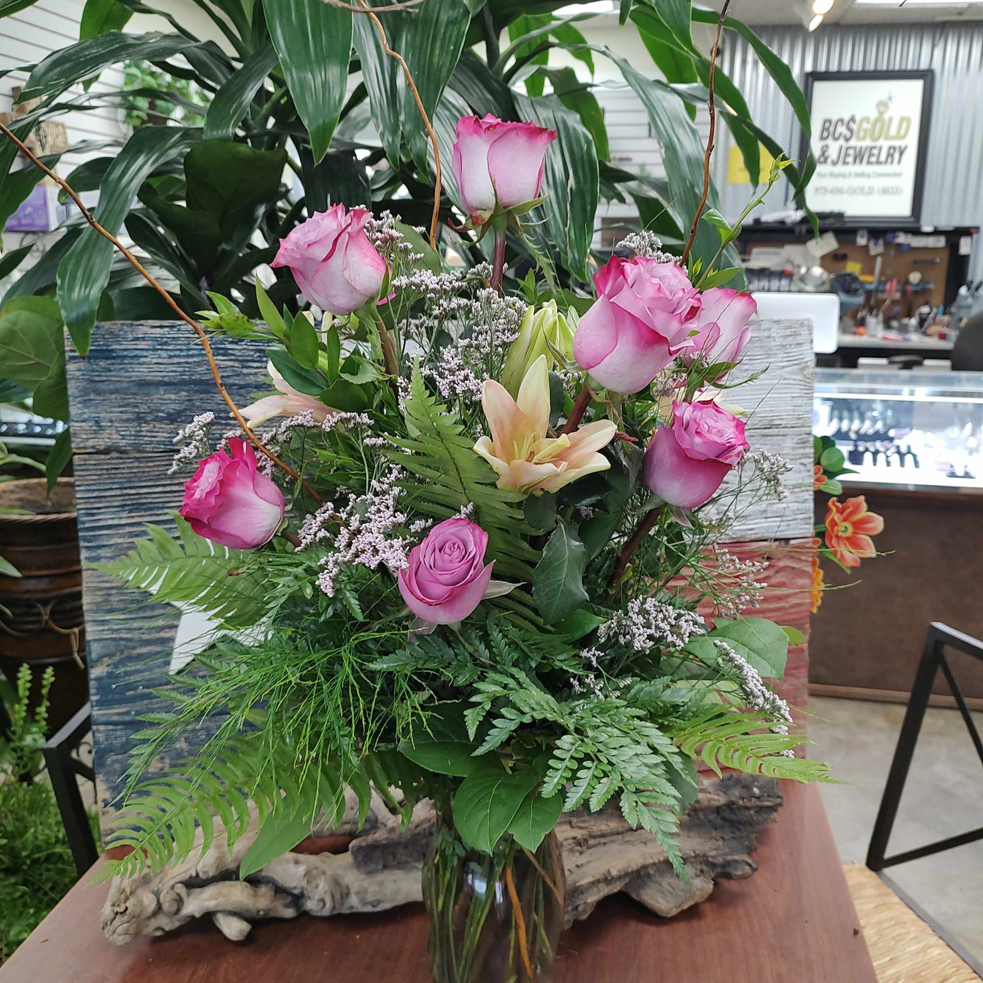 Tall arrangement of pink roses and peach lilies with filler blooms in a clear glass vase