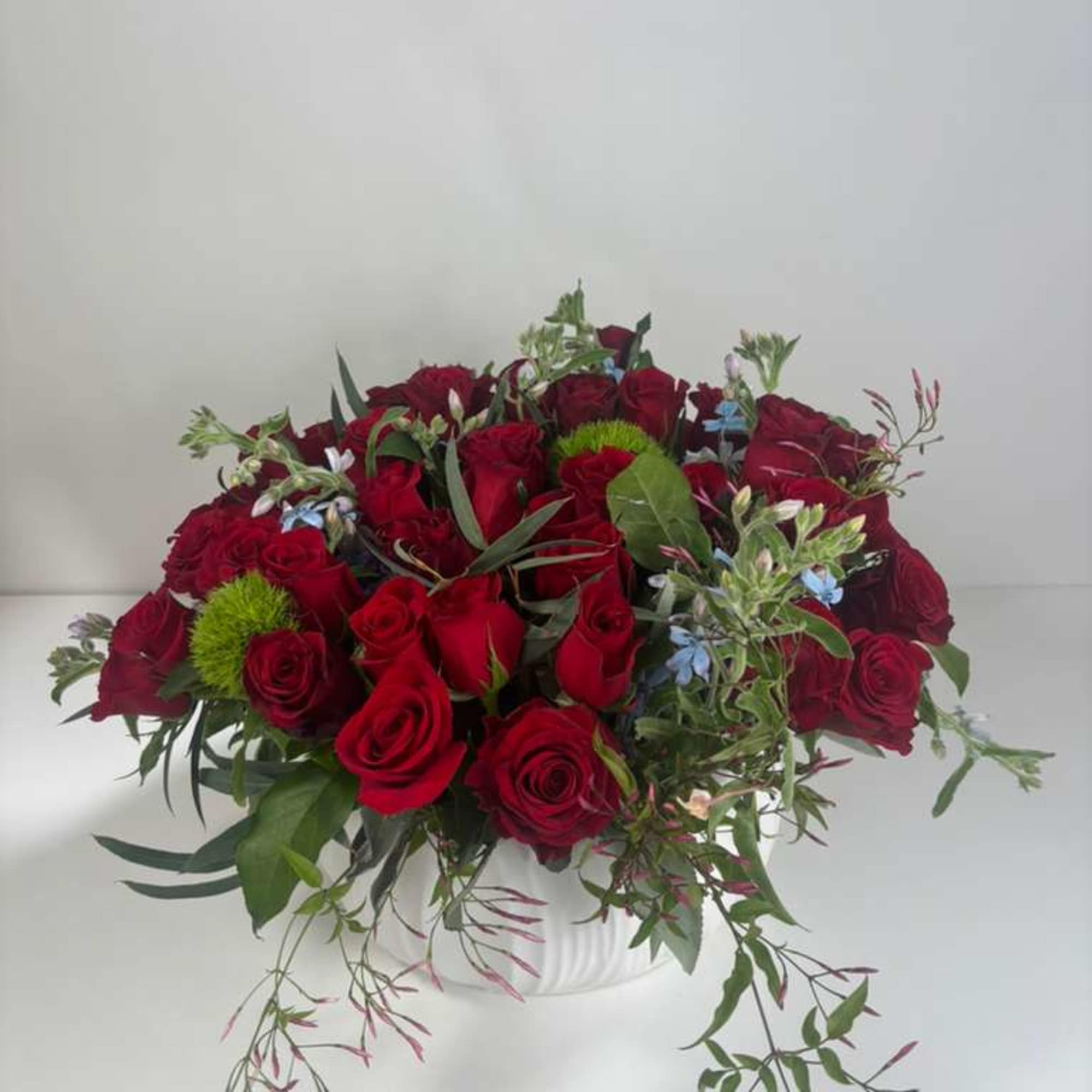 Red rose arrangement in a white vase with trailing greenery