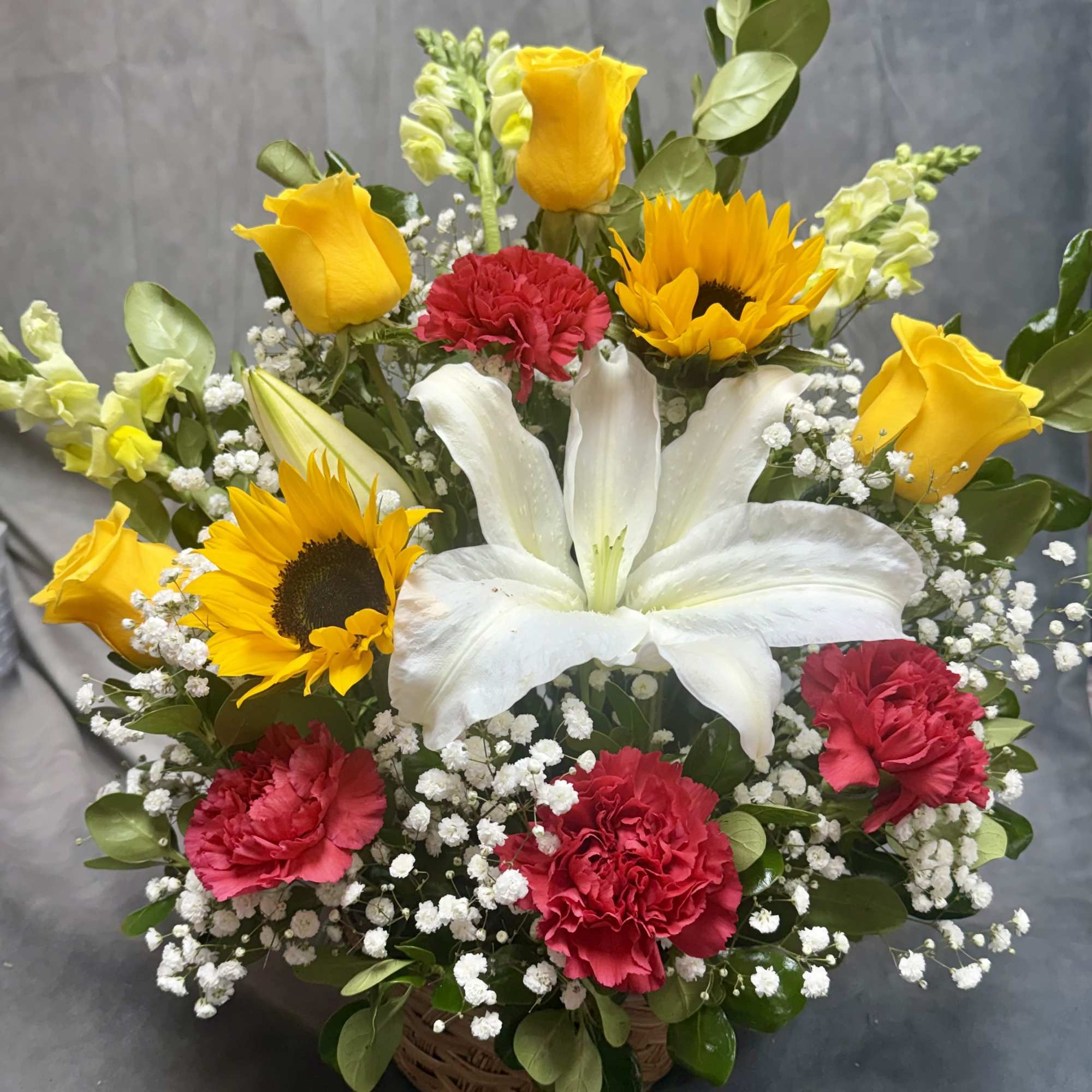 Basket arrangement with white lily, yellow roses, sunflowers, and red carnations