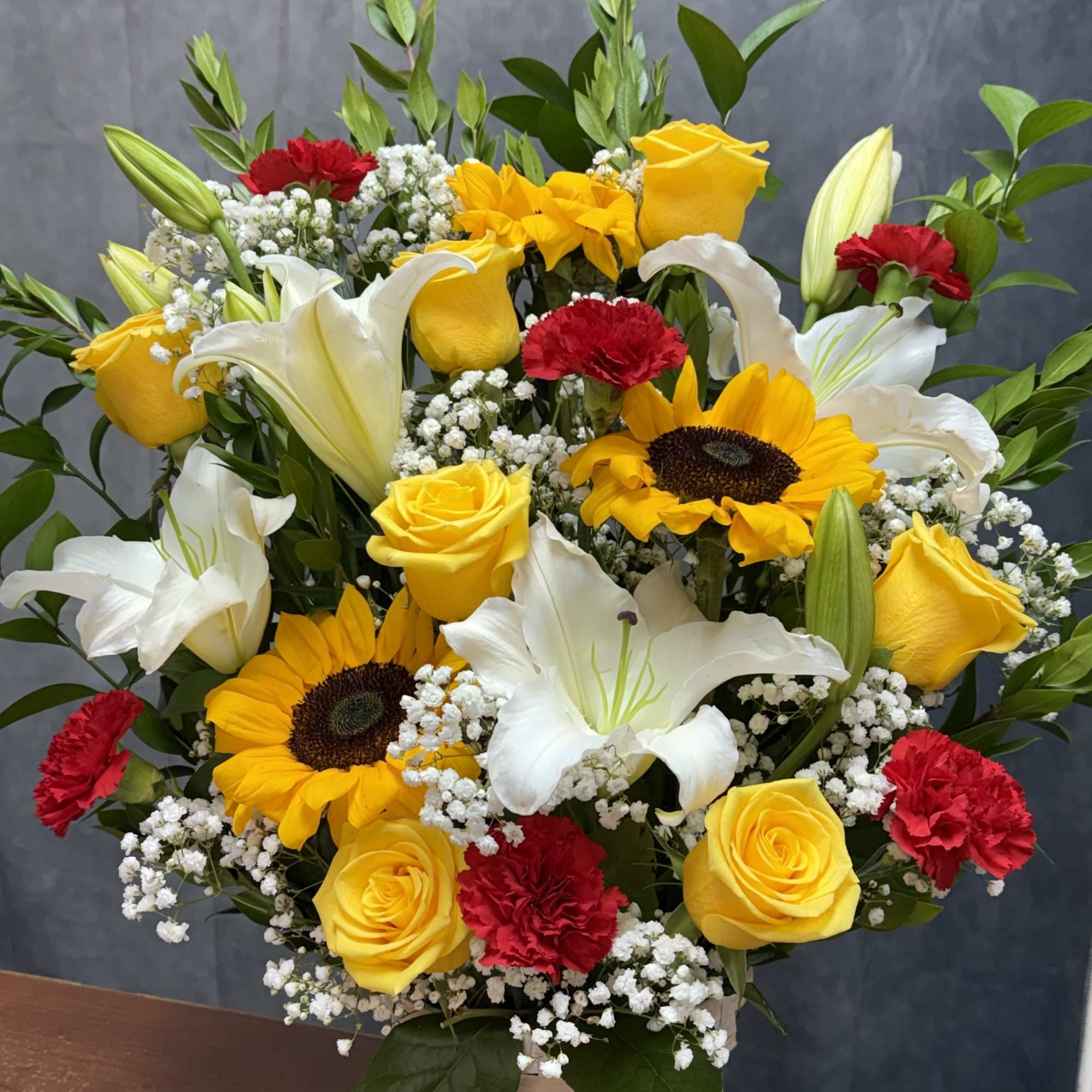A cheerful blend of golden sunflowers, yellow roses, red carnations, and a