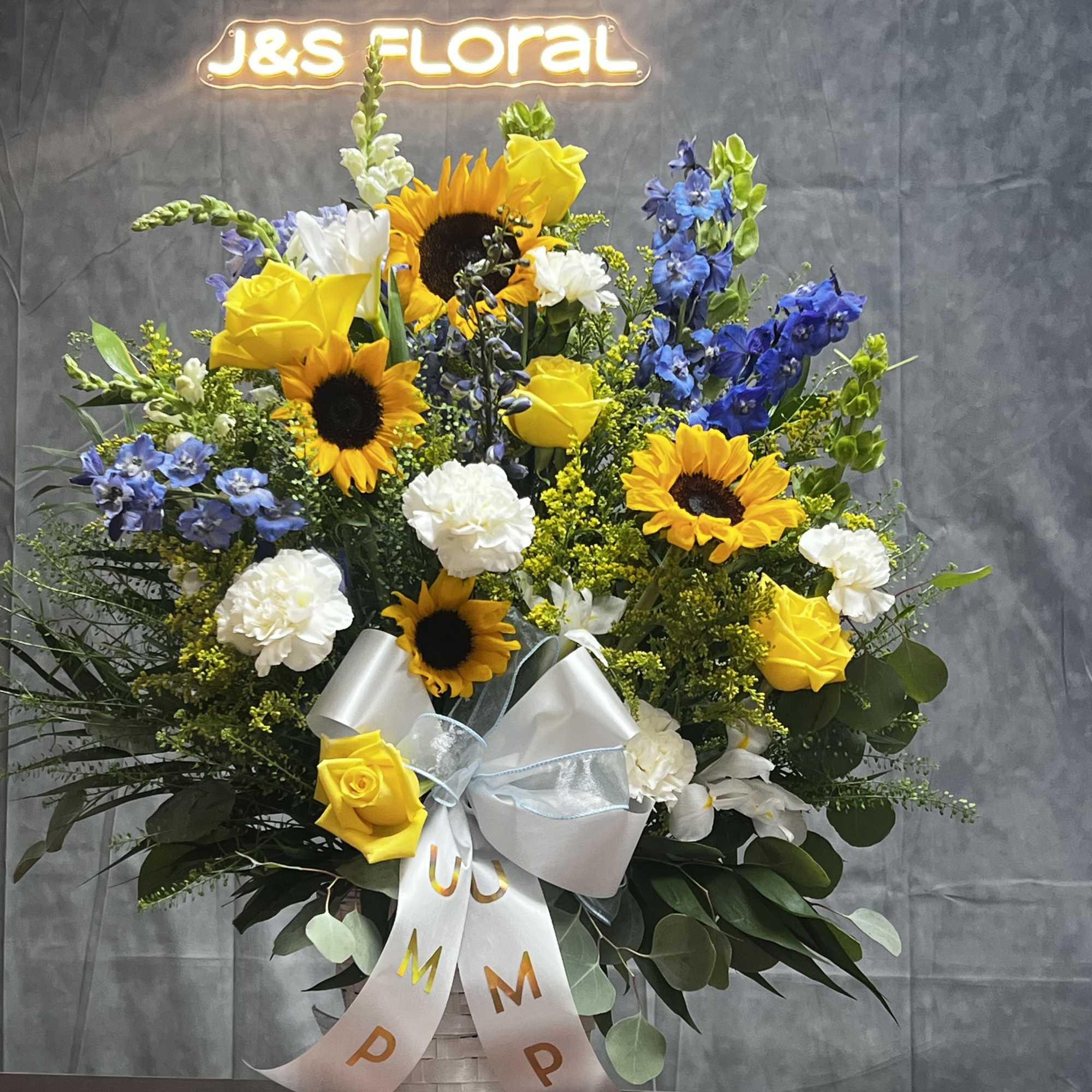 Basket arrangement with sunflowers, yellow roses, white carnations, and blue flowers