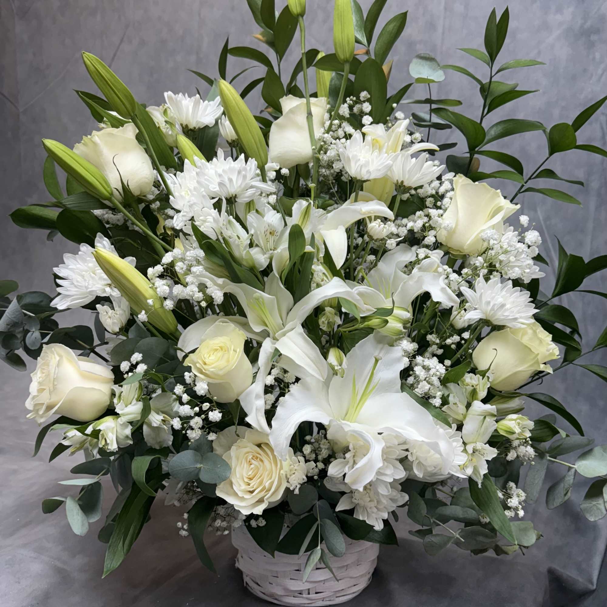 White lilies and roses arranged in a white basket