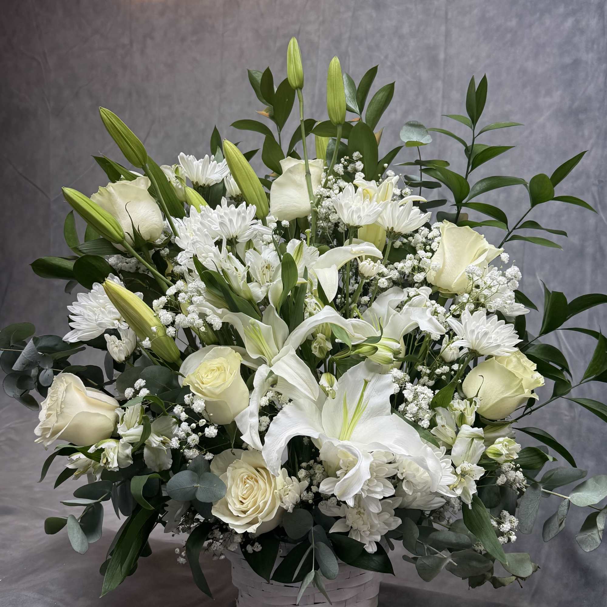 White lilies and roses arranged in a basket with greenery