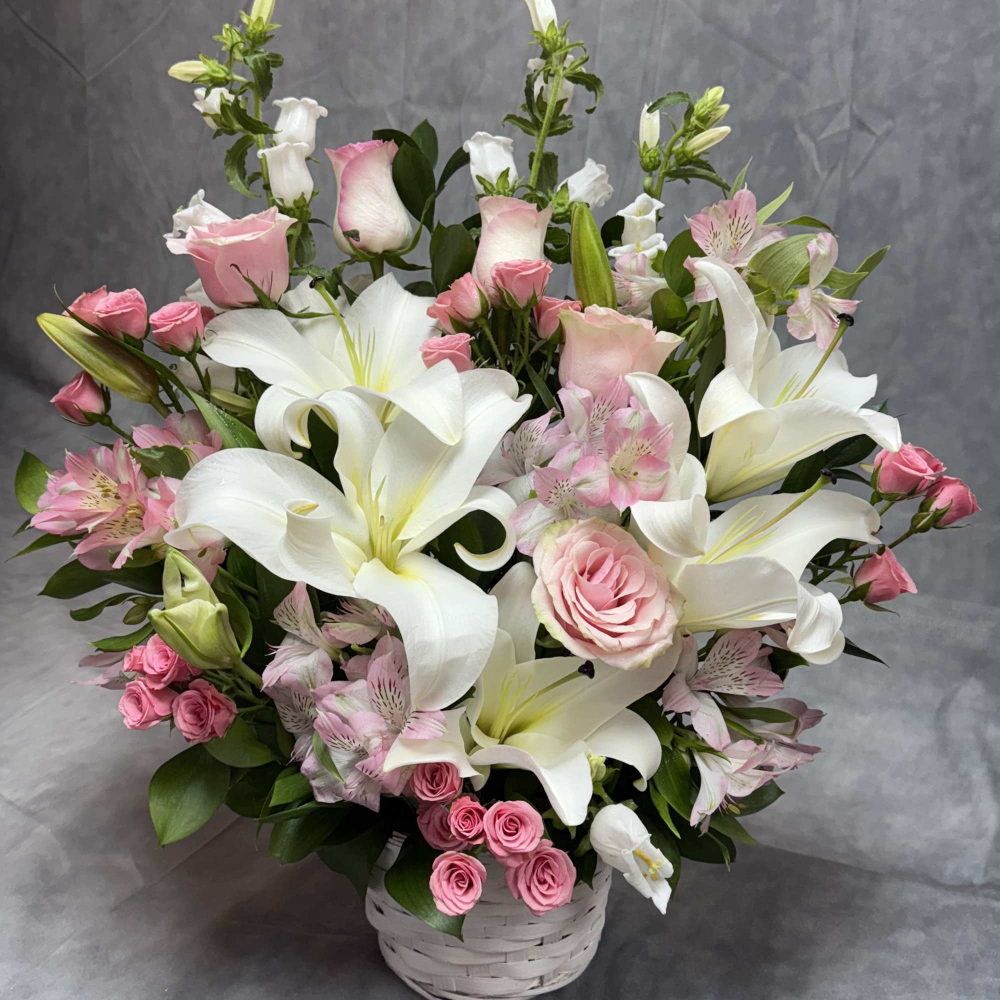 Pink roses and white lilies arranged in a white basket