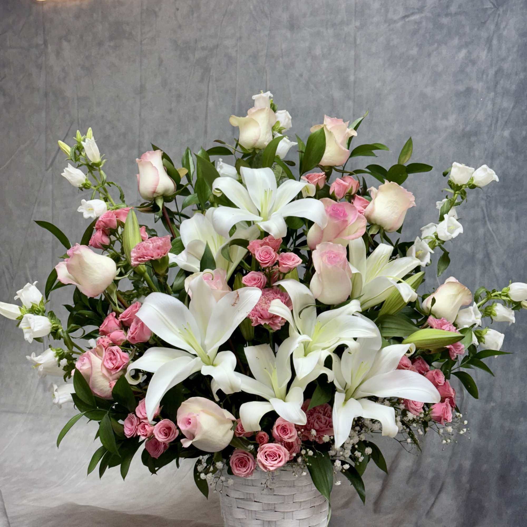 Pink roses and white lilies arranged in a white basket