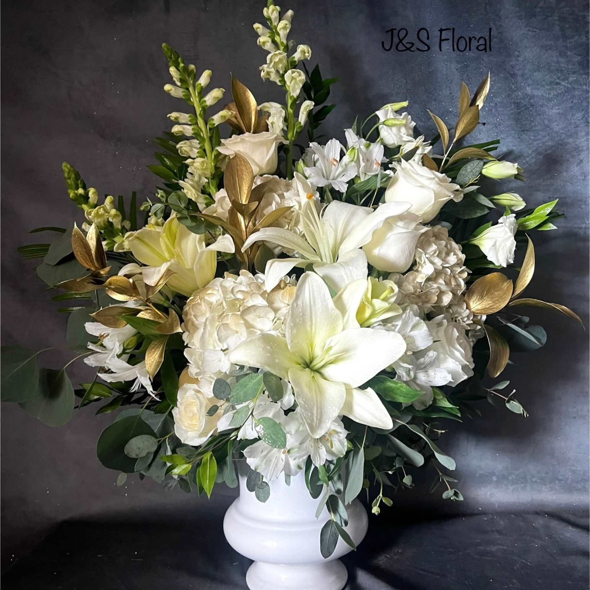 White floral arrangement in a white pedestal vase with gold foliage accents