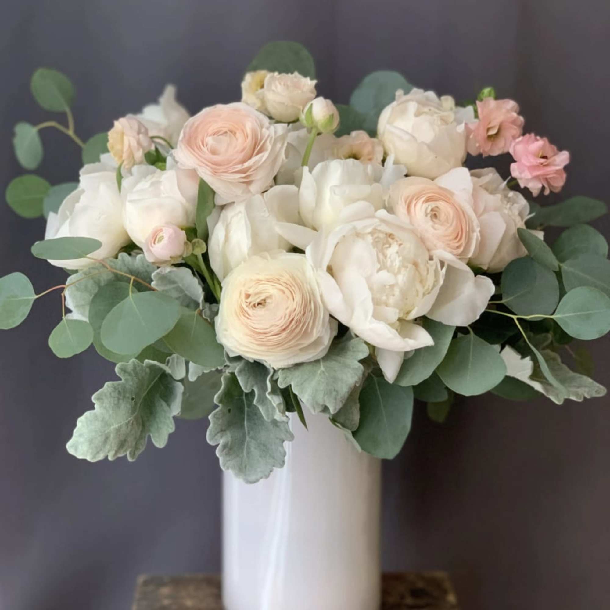 Blush and white bouquet in a white vase with round green foliage
