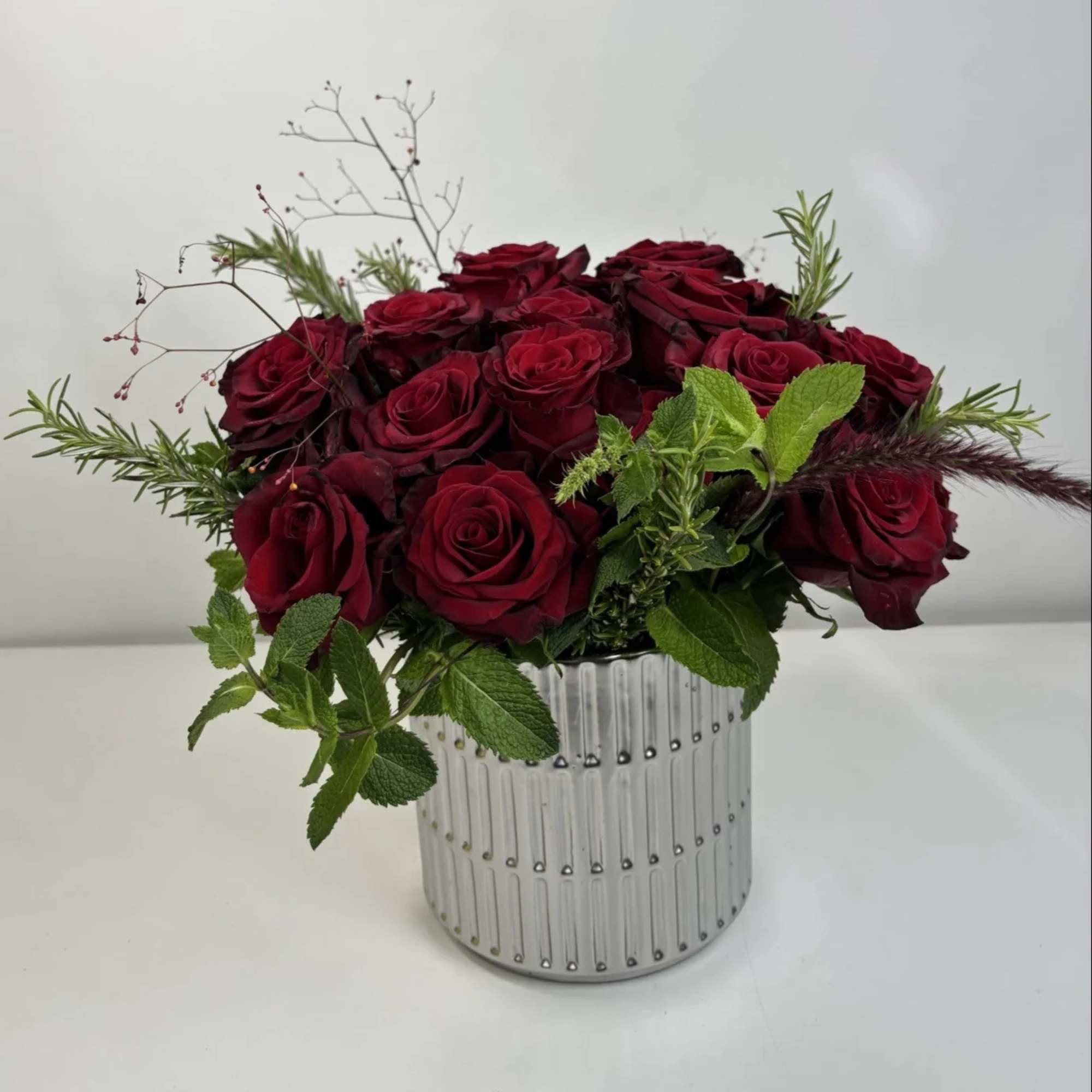 Red rose arrangement in a ribbed silver vase with green accents