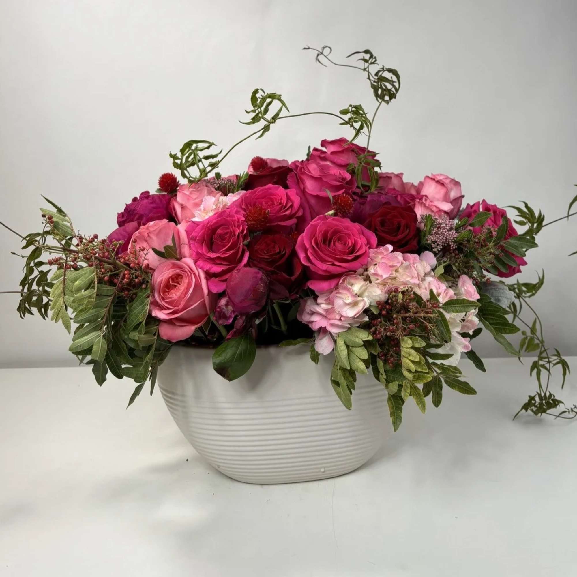 Pink and red rose arrangement in a white ceramic bowl vase