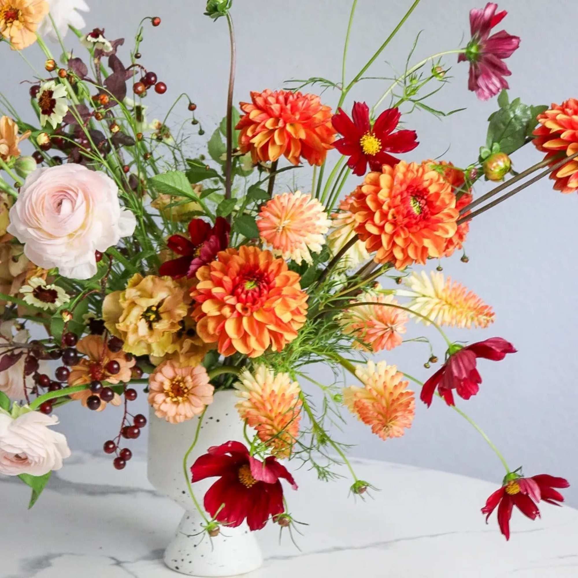 Mixed bouquet in a white vase with orange, red, and pale pink flowers