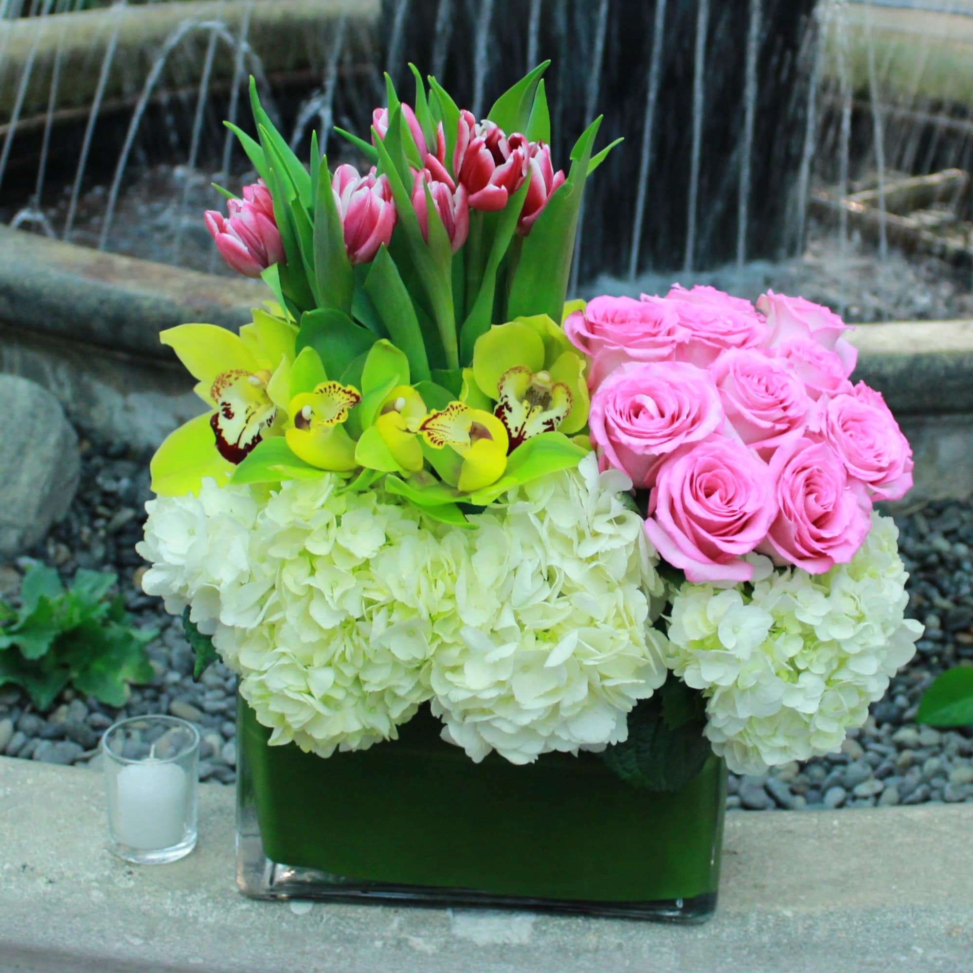 Pink roses, tulips, orchids, and white hydrangeas in a glass vase