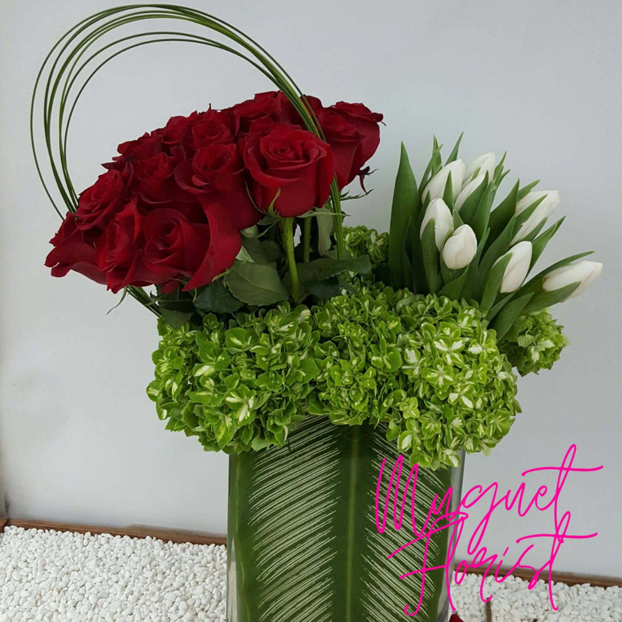 Red roses and white tulips in a tall green vase with green hydrangeas