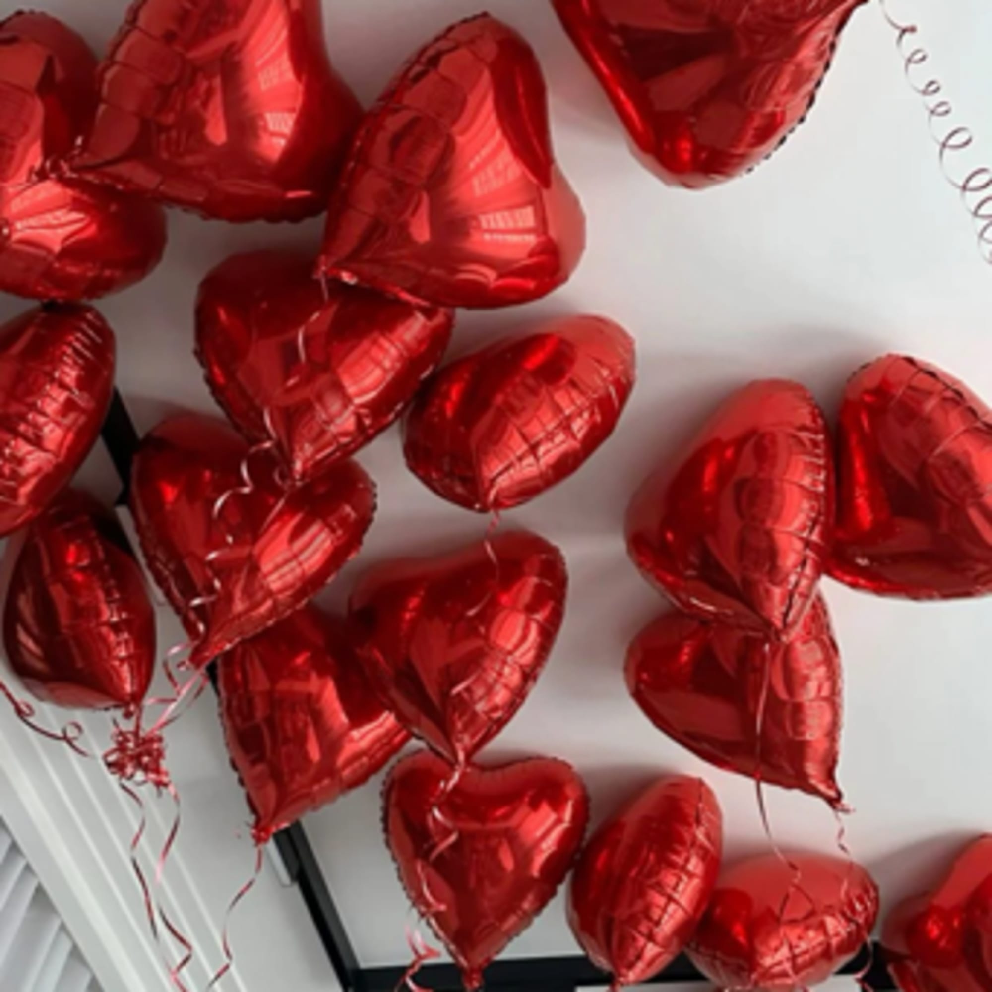 Cluster of red heart-shaped balloons with curling ribbons on a ceiling