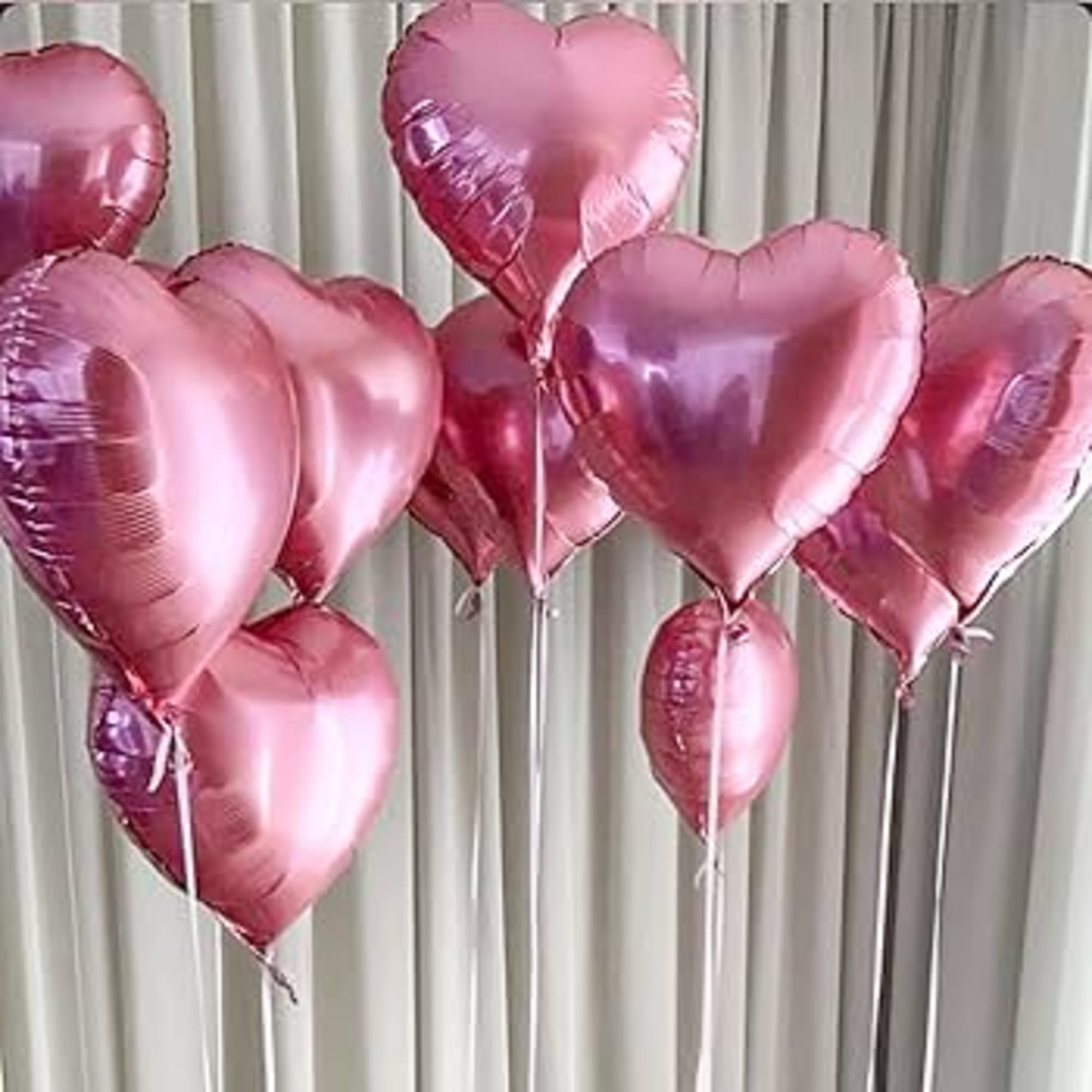 Cluster of pink heart-shaped balloons against a curtain backdrop