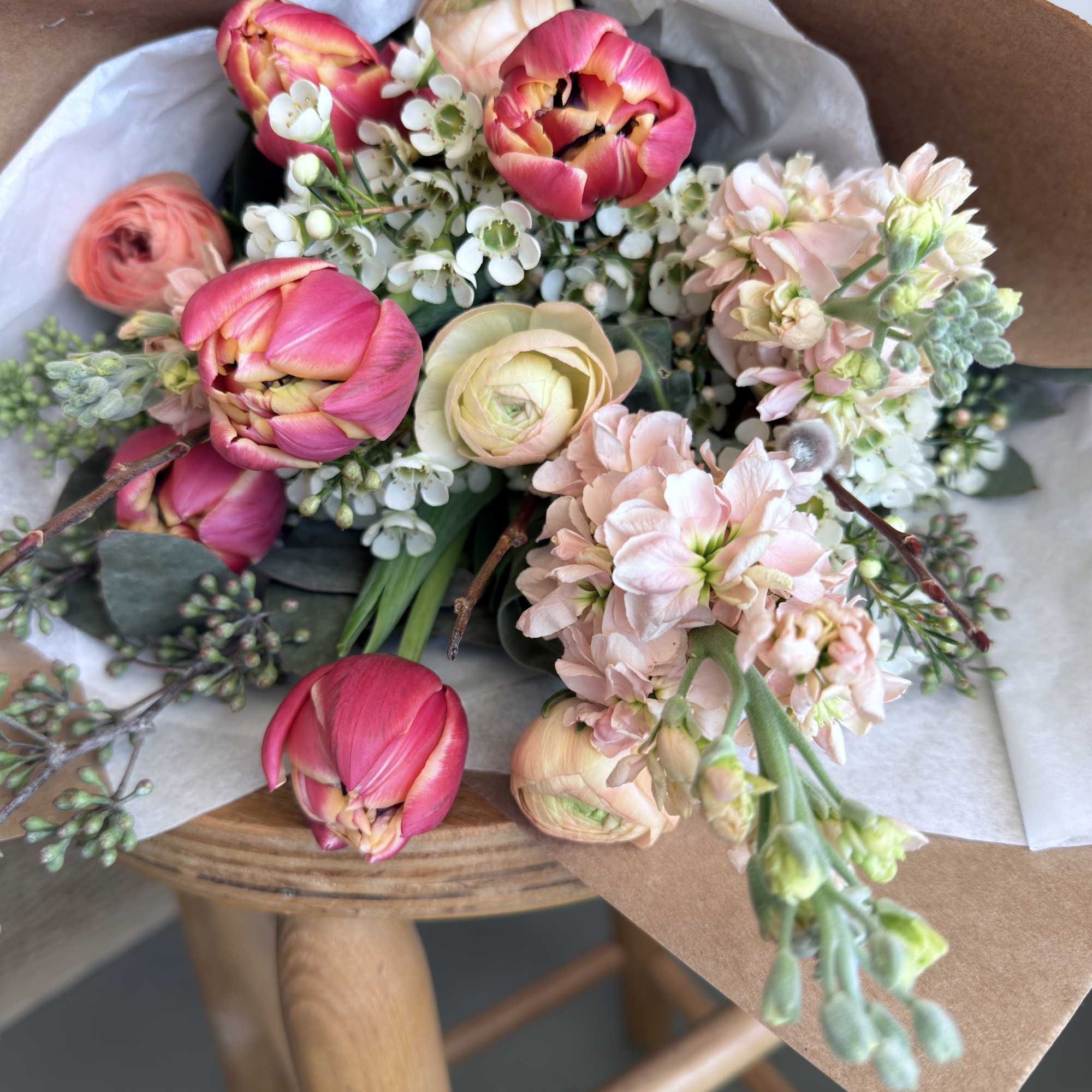 Bouquet of pink tulips and pale peach flowers wrapped in brown paper