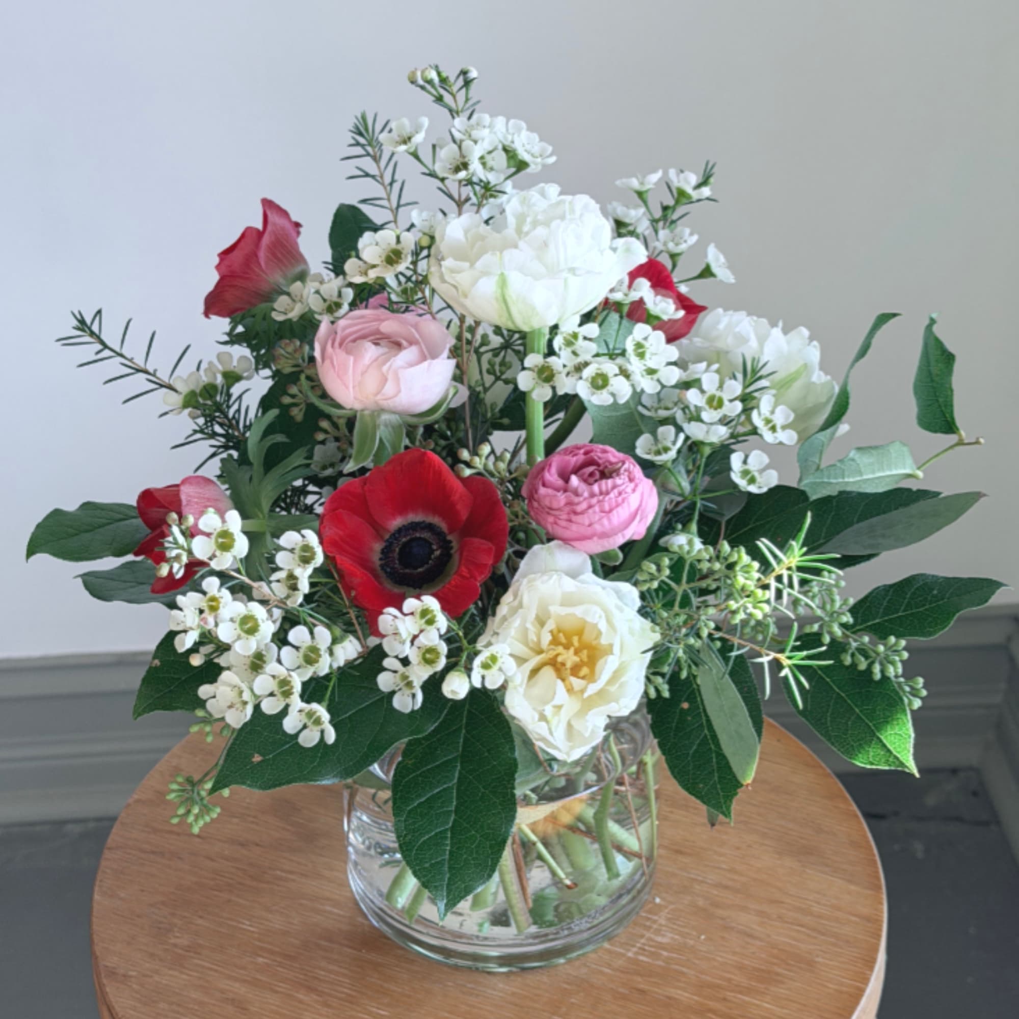 Mixed arrangement of red, pink, and white flowers in a clear glass vase on a wooden table
