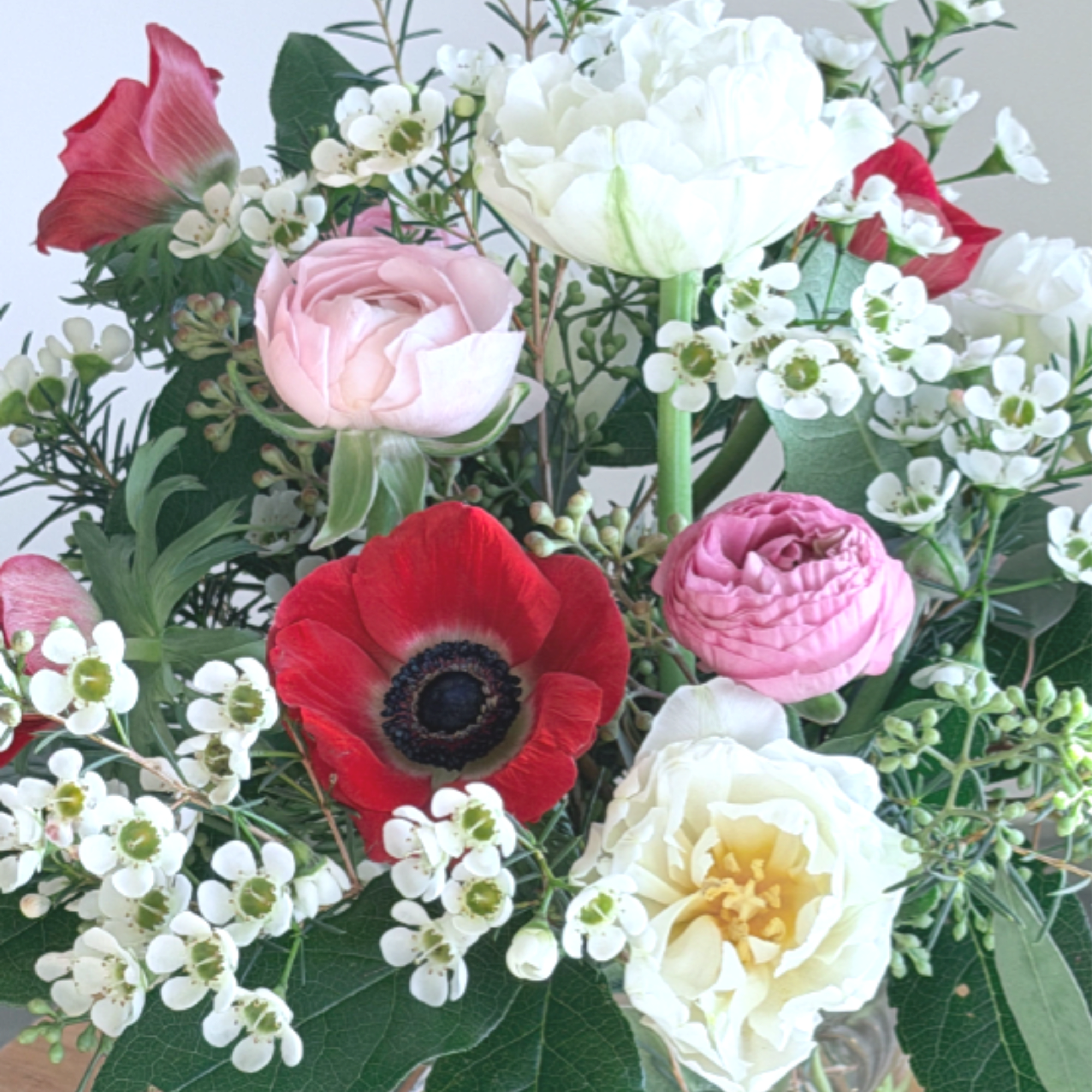 Mixed bouquet of red anemone, pink ranunculus, and white blooms in a clear glass vase