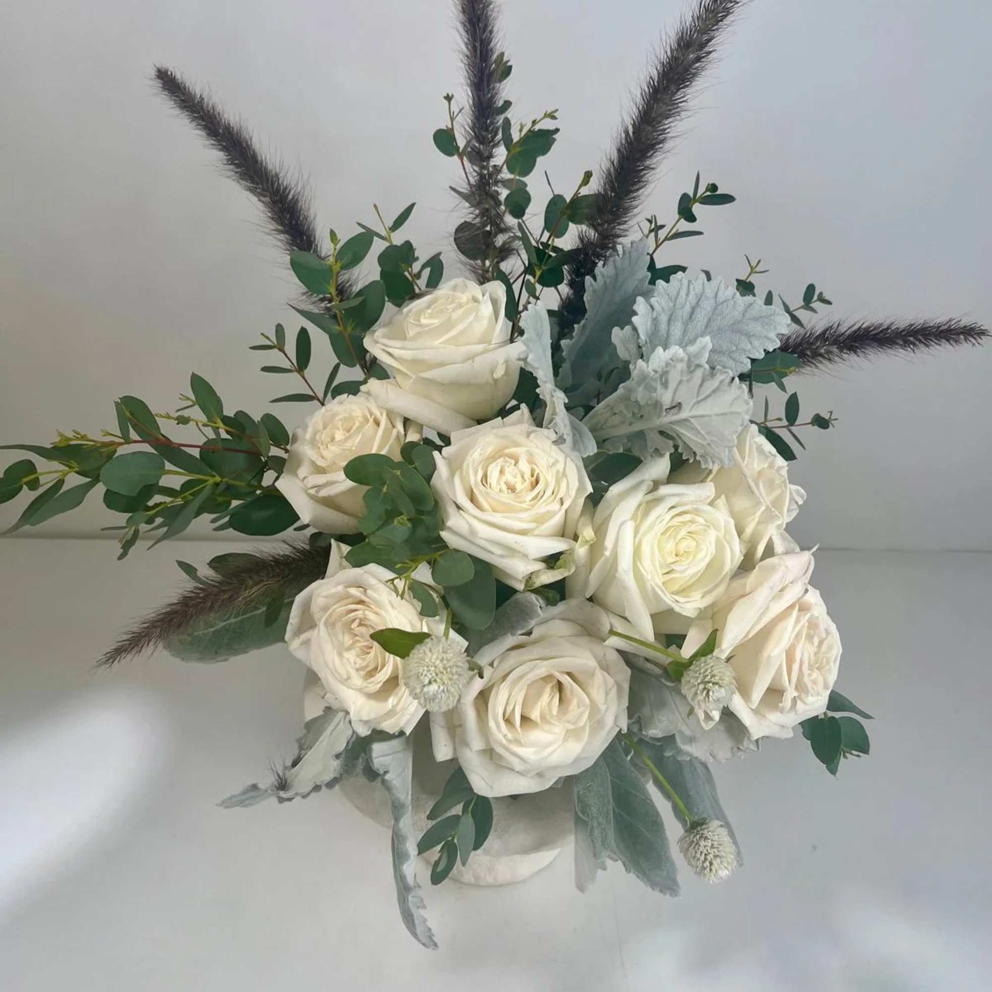 White rose bouquet with eucalyptus and dark feathery accents in a white container