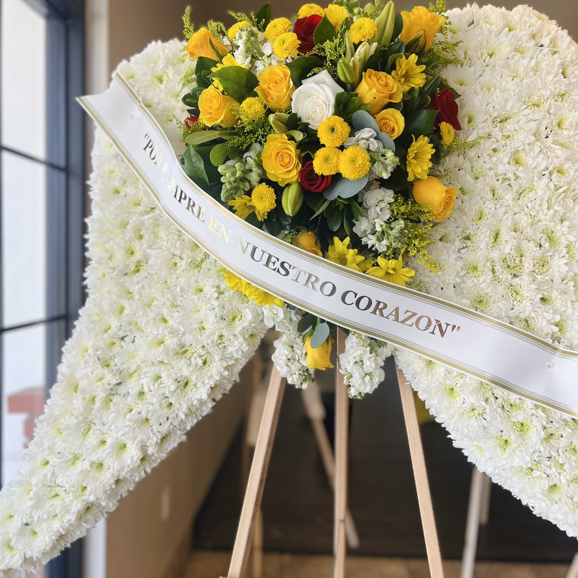 White funeral wreath with yellow and red roses on a wooden easel