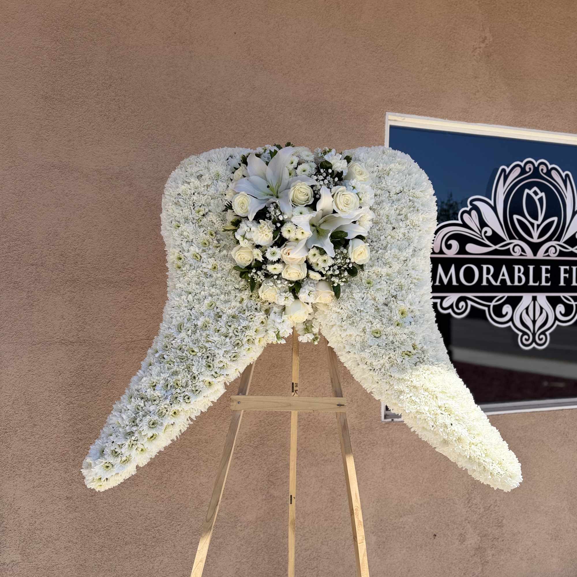 White floral standing spray on a wooden easel with roses and lilies