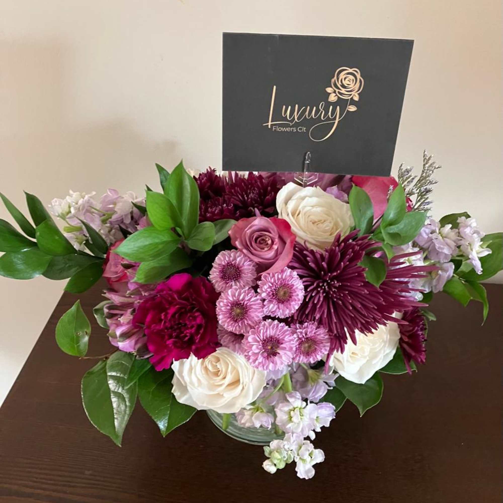 Mixed pink, white, and purple bouquet in a glass vase with a logo card