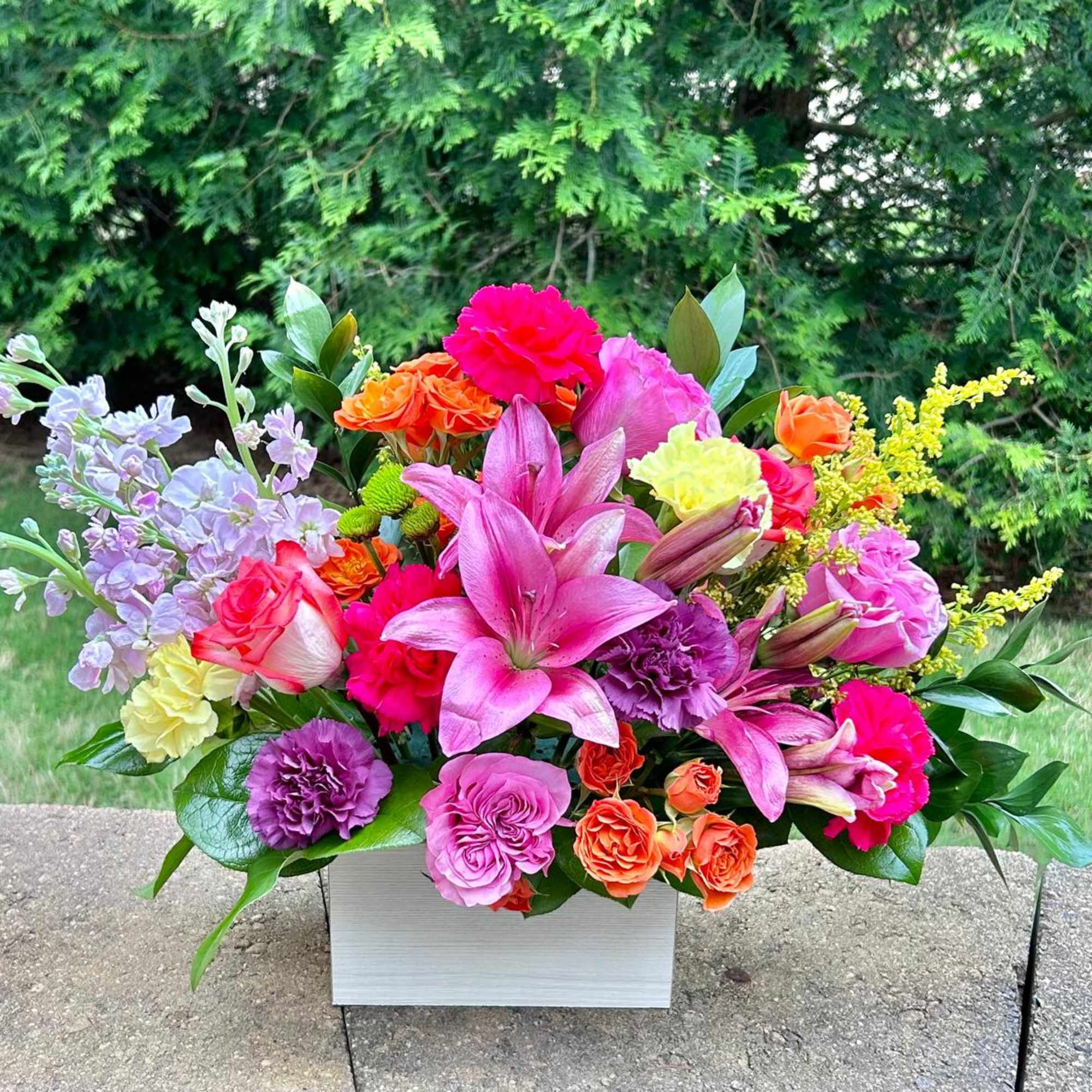 Bright mixed bouquet in a white rectangular vase with pink lilies and roses
