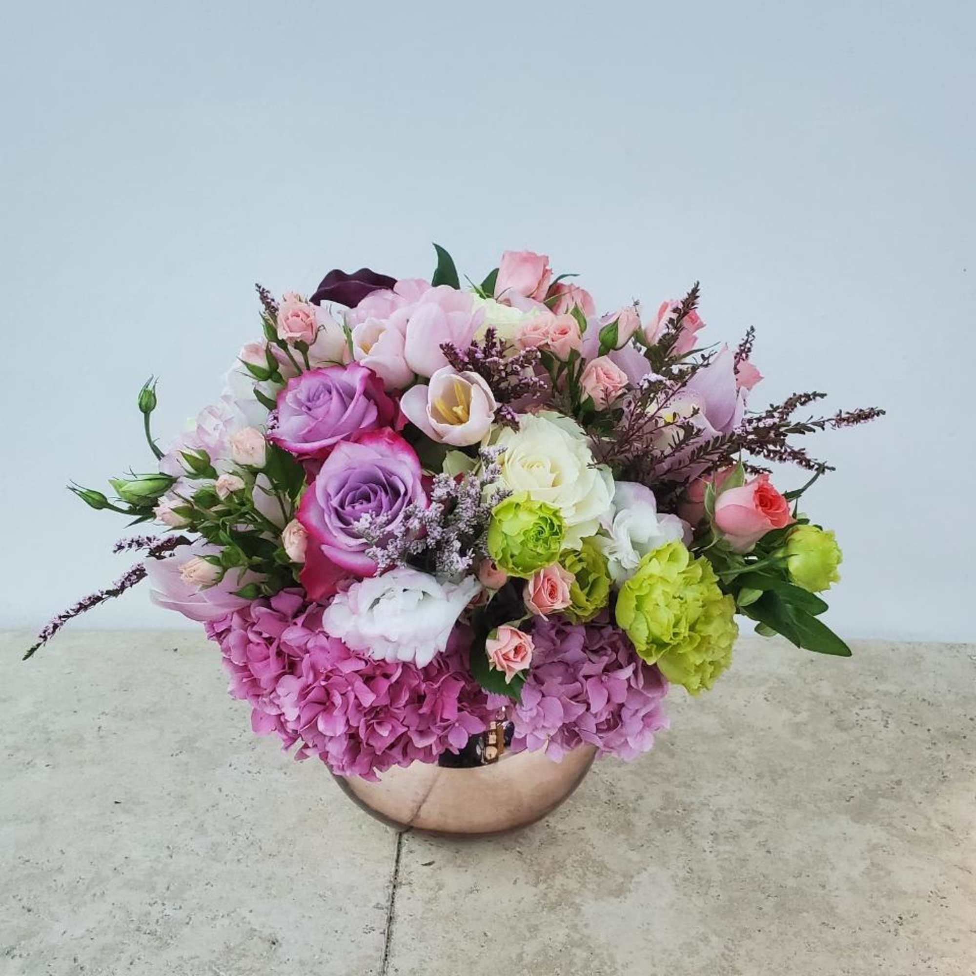 Mixed pink and purple flower arrangement in a round metallic vase