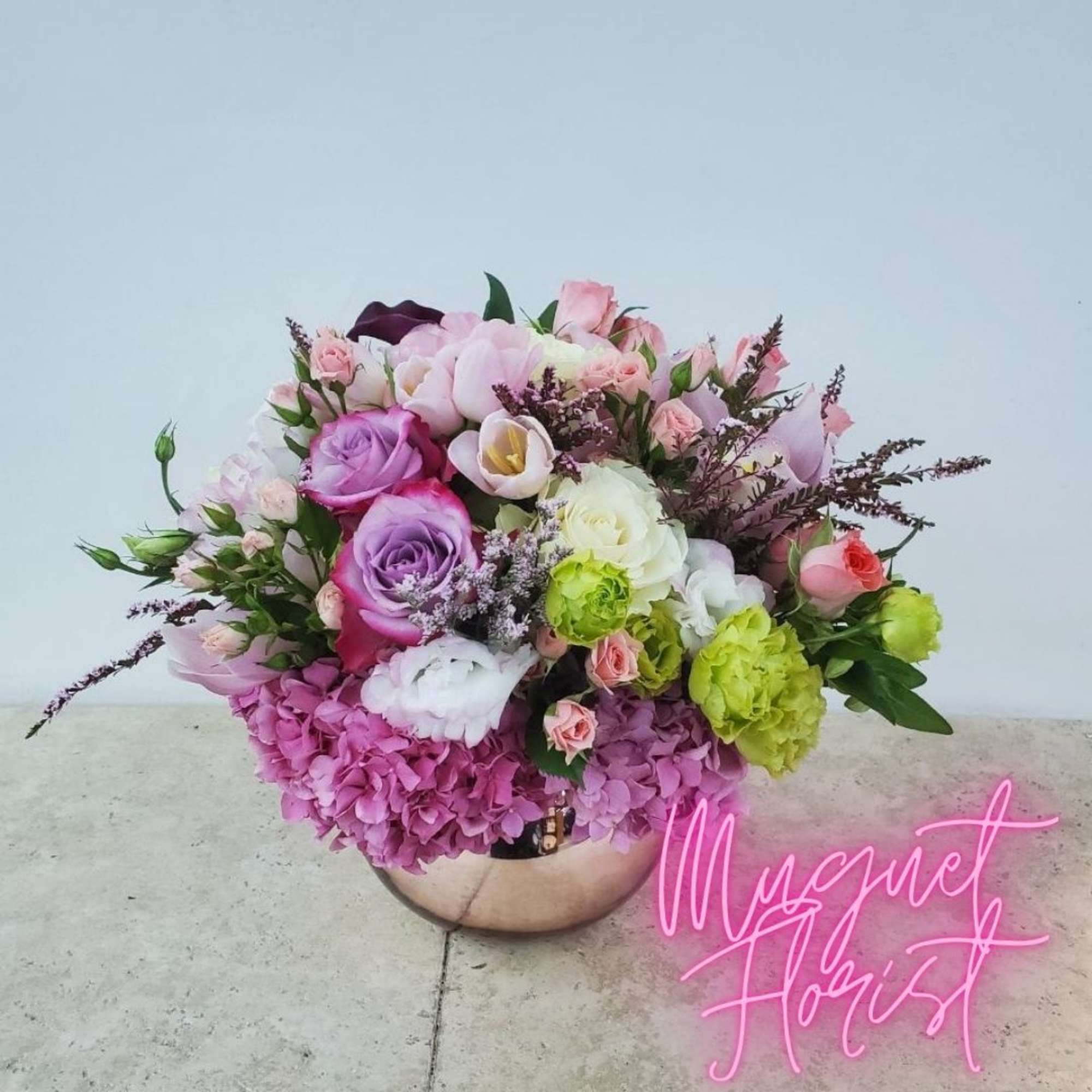 Mixed pink, purple, and white flower arrangement in a round vase