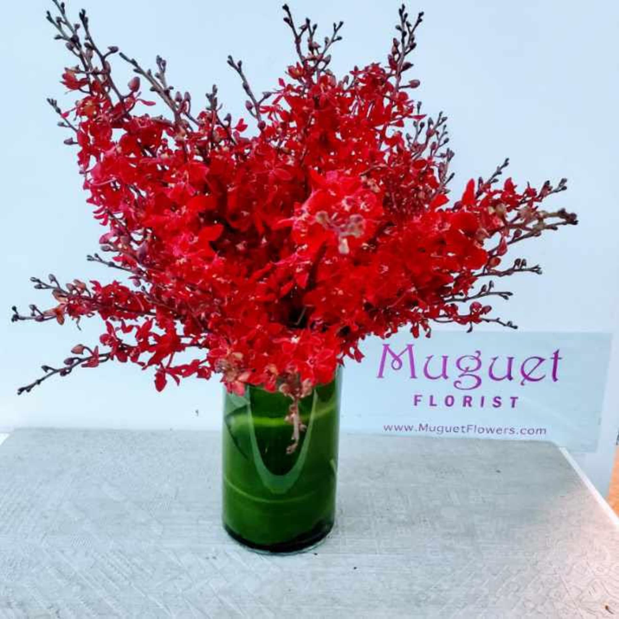 Red orchid arrangement in a green glass vase