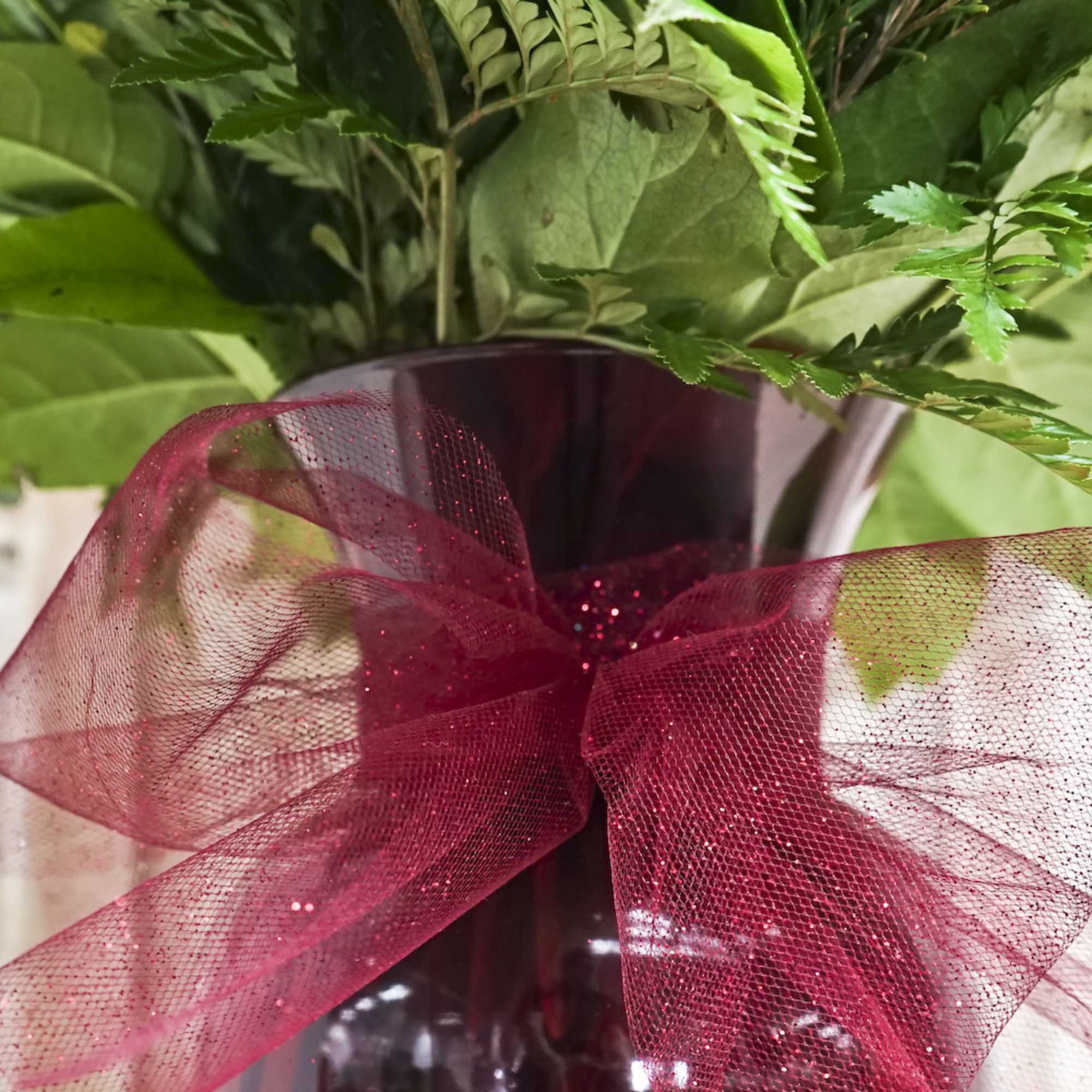 Green foliage in a dark vase with a red ribbon bow