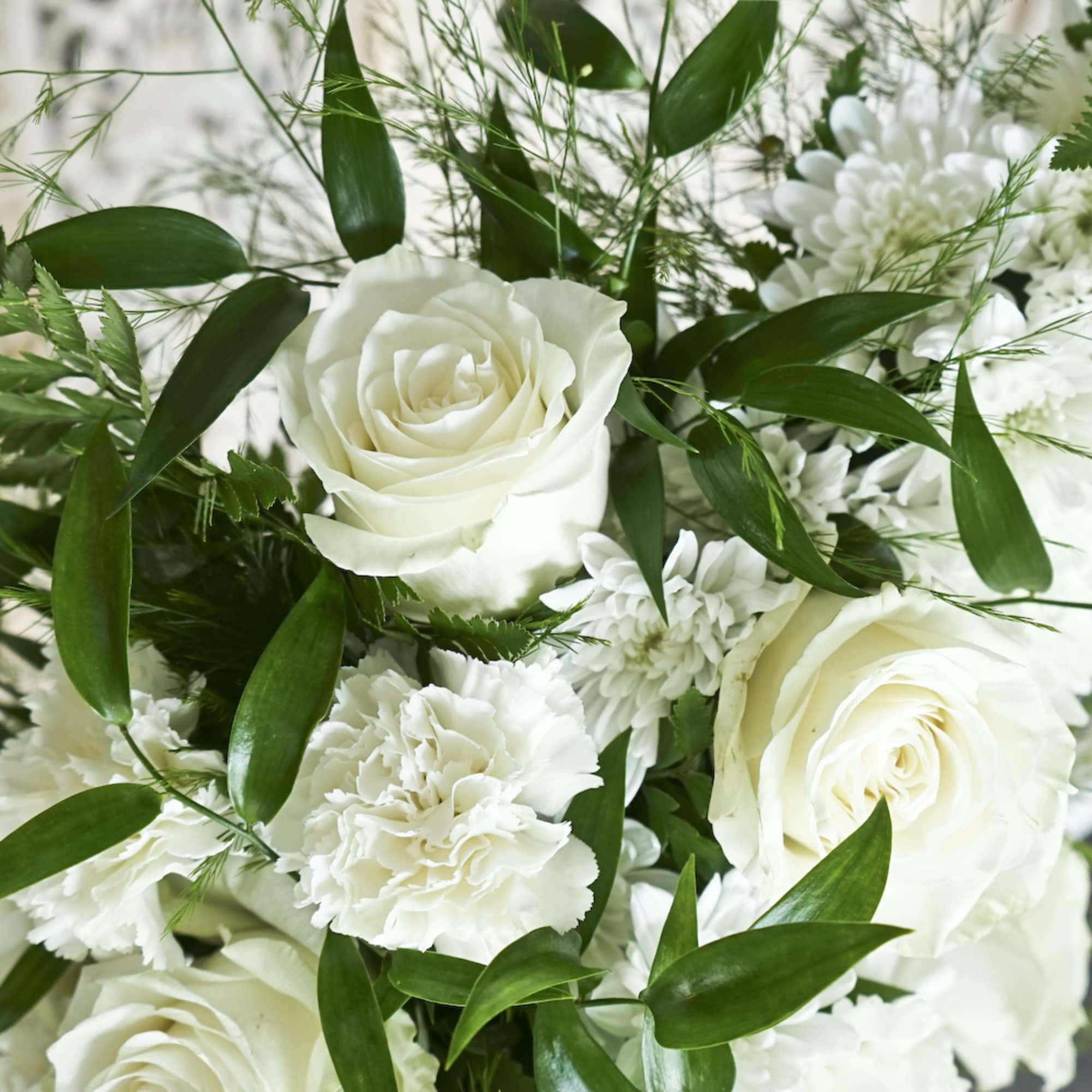 White roses and carnations arranged with green foliage