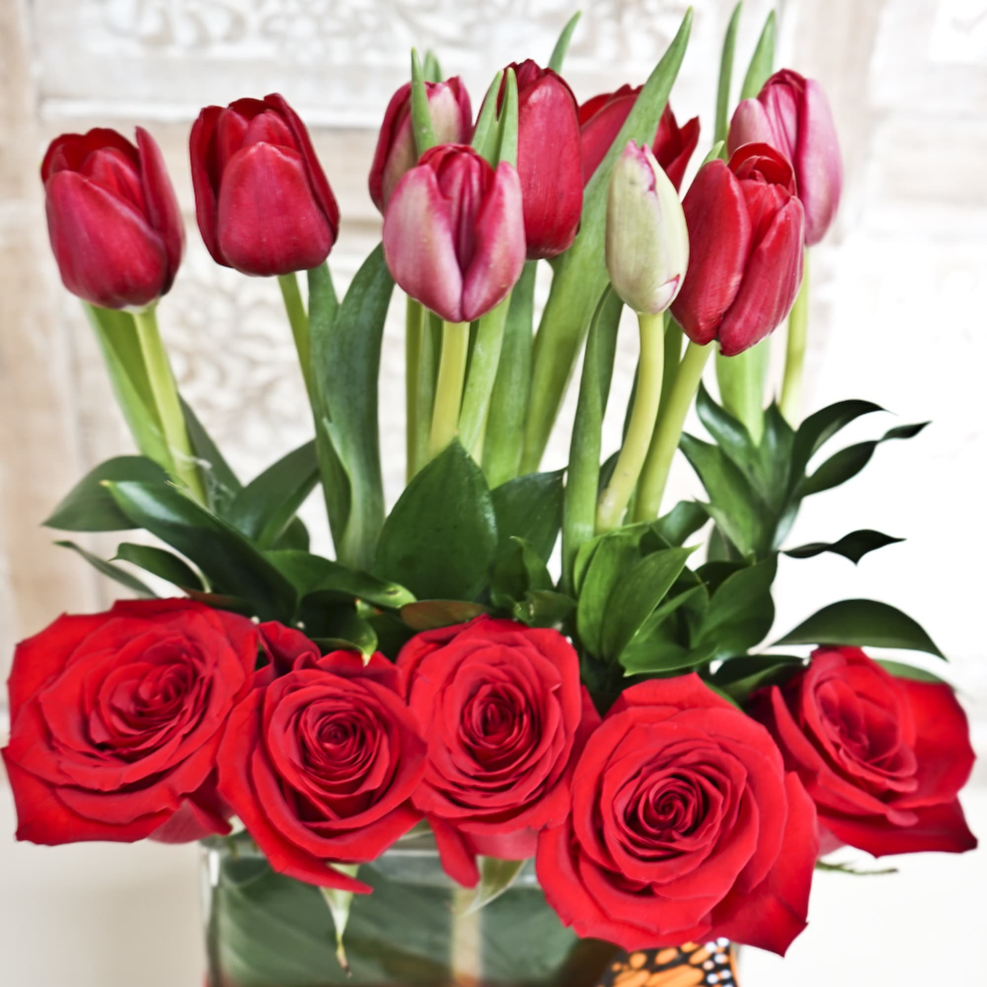 Red roses and pink tulips arranged in a glass vase