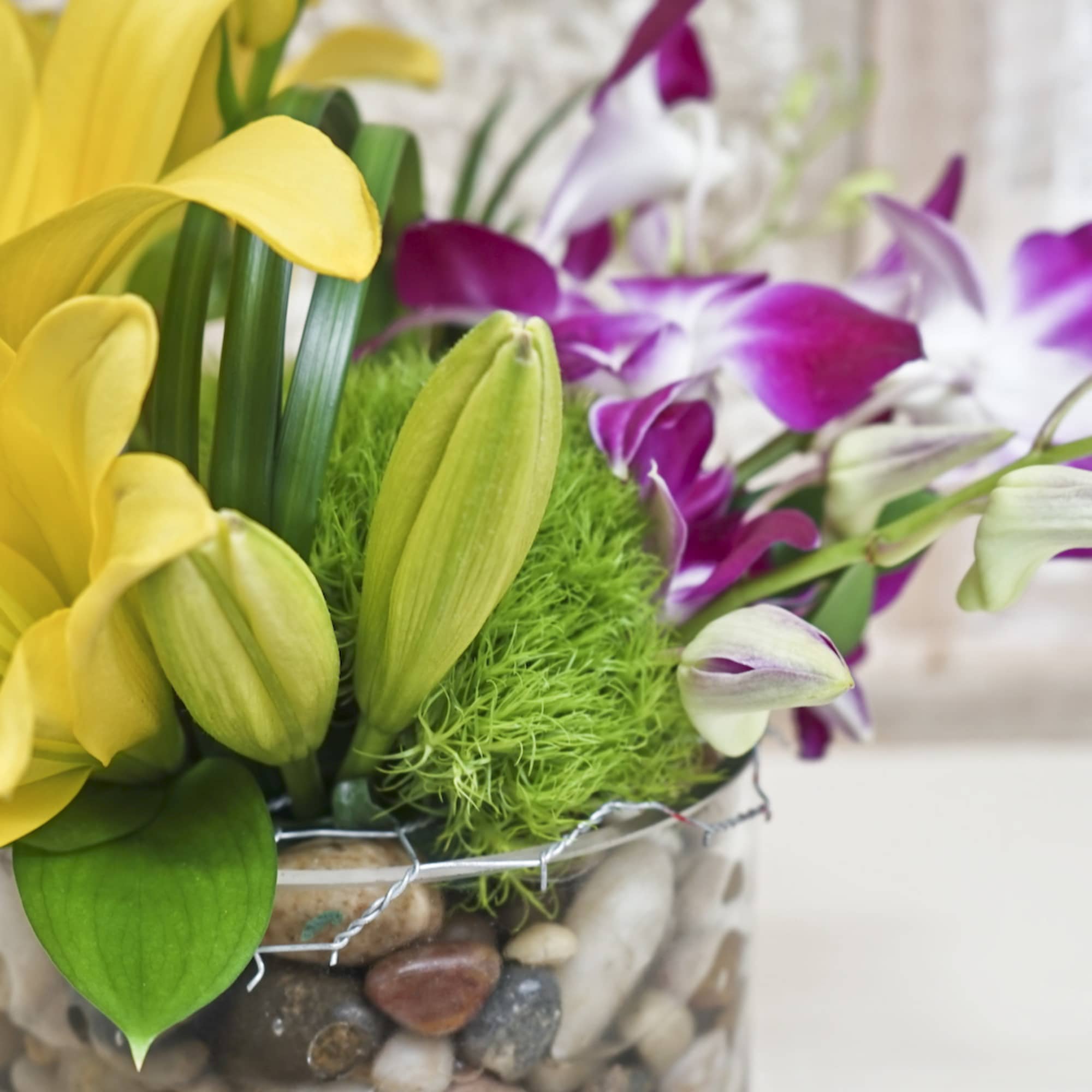 Yellow and purple lilies in a glass vase with decorative stones