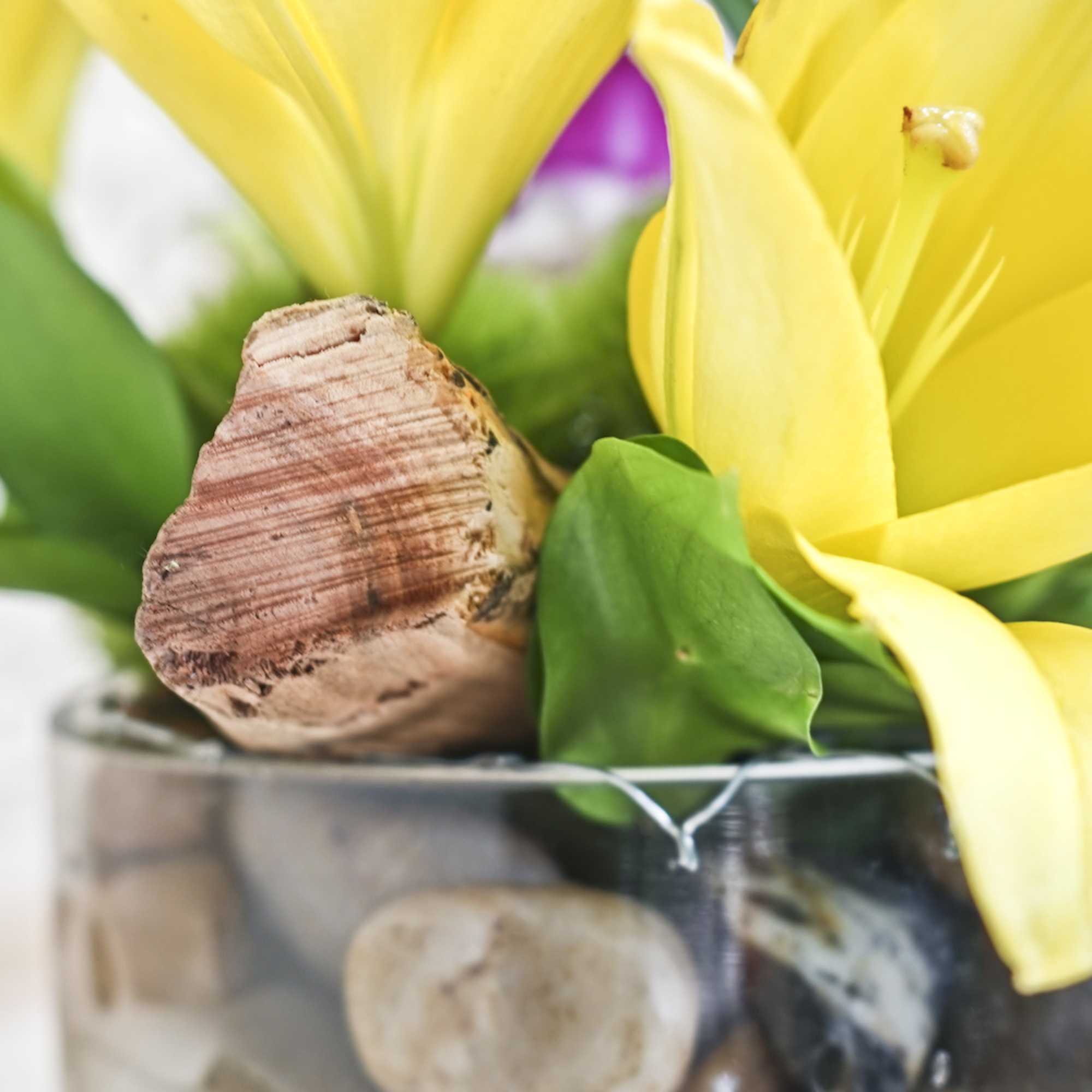 Close-up of yellow lilies in a glass vase with a decorative wood accent