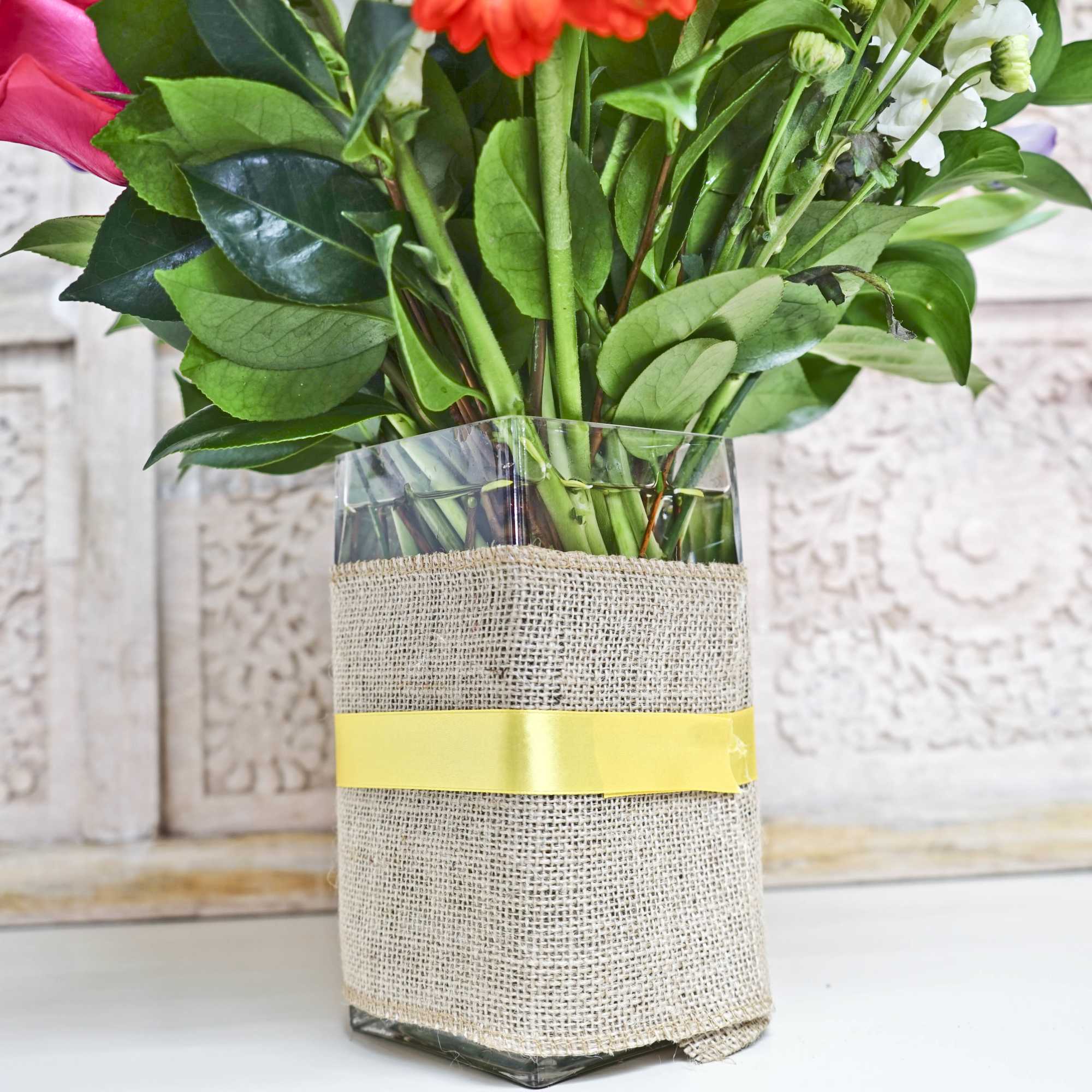 Pink and white flowers in a glass vase wrapped with burlap and yellow ribbon